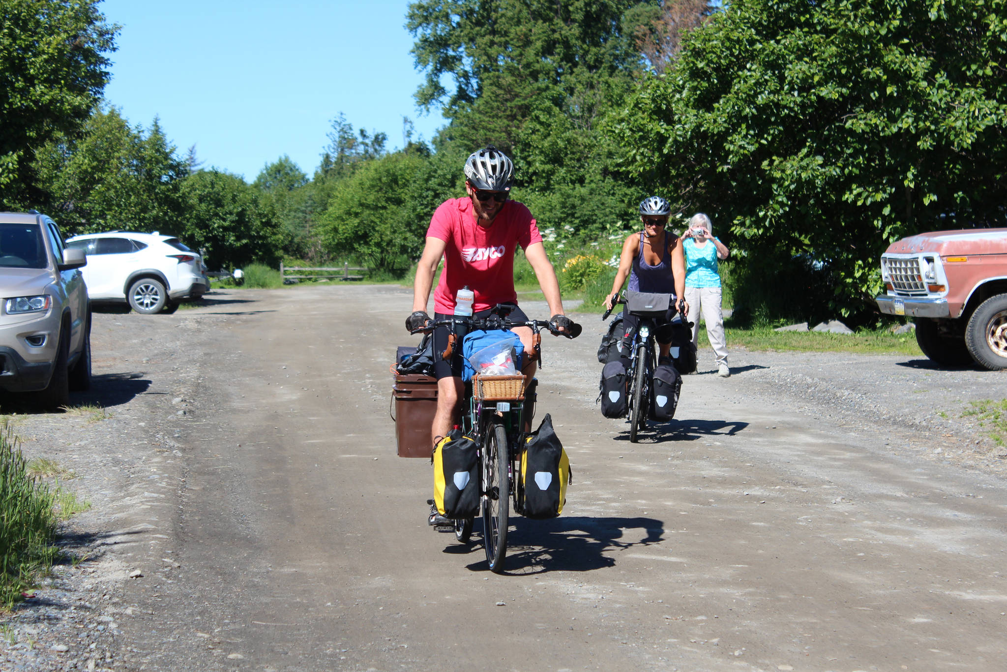 Chris Haag and Sophie George take off on their bikes from a rental on Hidden Way, with Haag’s grandmother taking a photo as they go, on Monday, July 2, 2018 in Homer, Alaska. The husband and wife are traveling by bike from Alaska to Argentina, a trip estimated to take two years. (Photo by Megan Pacer/Homer News)