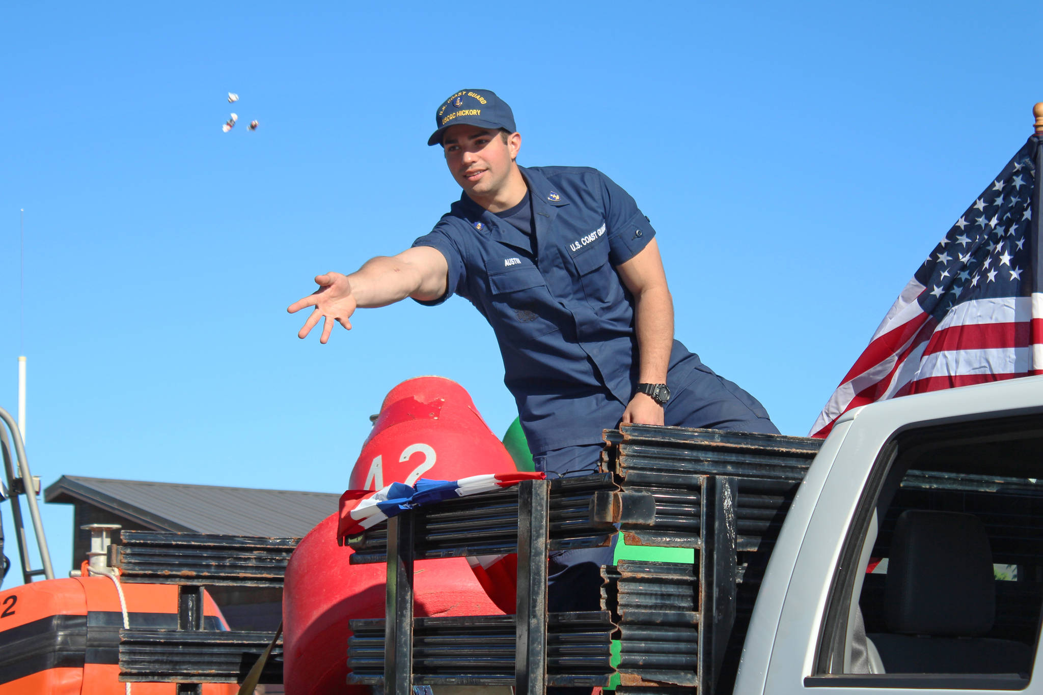 A member of the U.S. Coast Guard tosses candy to children and families lining Pioneer Avenue during the annual Independence Day parade Wednesday, July 4, 2018 in Homer, Alaska. Coast Guard participants were representing the U.S. Coast Guard Cutter Hickory, also called the “Bull of the North.” (Photo by Megan Pacer/Homer News)