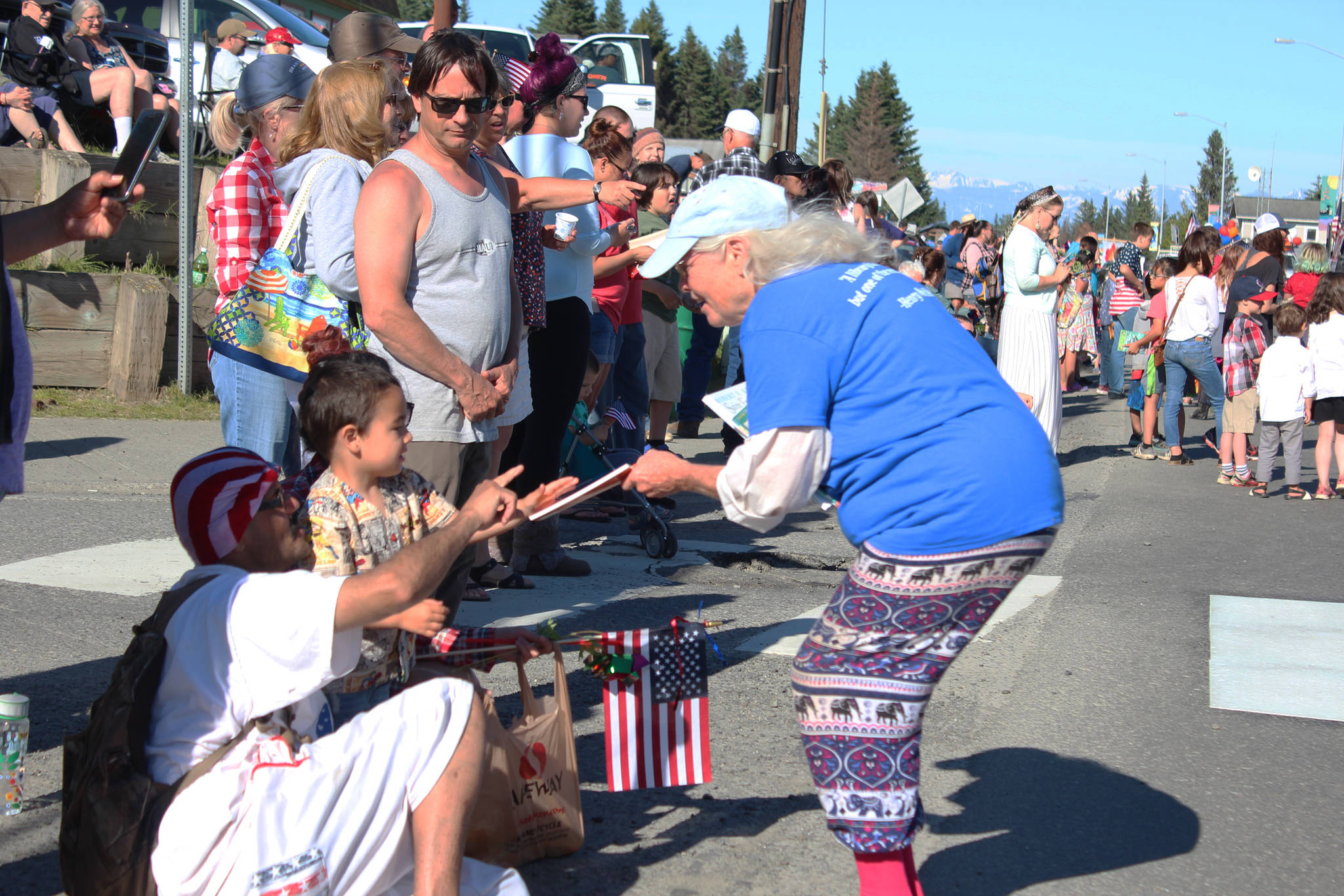 A member of the Friends of the Homer Library hands a book to a young boy and his family on Pioneer Avenue during the annual Independence Day parade Wednesday, July 4, 2018 in Homer, Alaska. The library friends marched down the street pushing book shelves on wheels filled with various volumes to hand out to spectators. (Photo by Megan Pacer/Homer News)