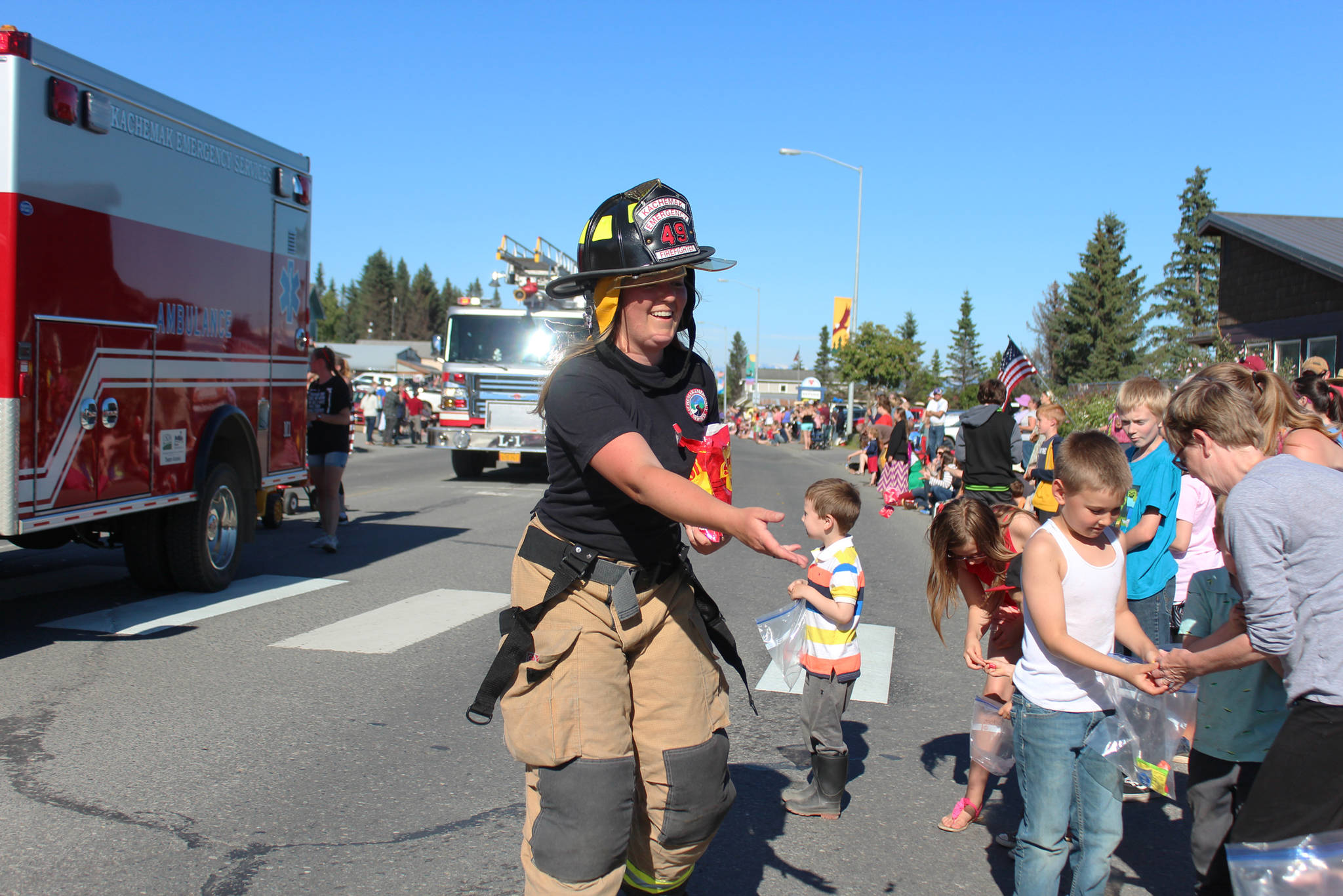 A member of Kachemak Emergency Services tosses candy to eager children along Pioneer Avenue during this year’s Independence Day parade Wednesday, July 4, 2018 in Homer, Alaska. (Photo by Megan Pacer/Homer News)