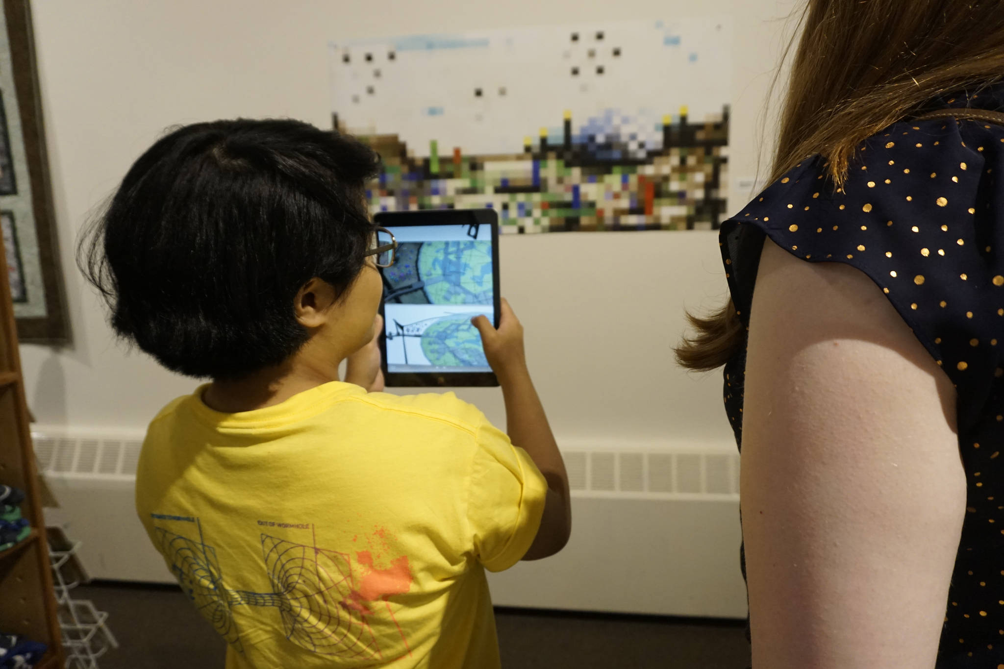Chloe Adkison views an image in an iPad from the “Dirigibles of Denali” show at the Pratt Museum at the July 6, 2018 First Friday opening in Homer, Alaska. The images appear when viewed through the HP Reveal augmented reality app. (Photo by Michael Armstrong/Homer News)