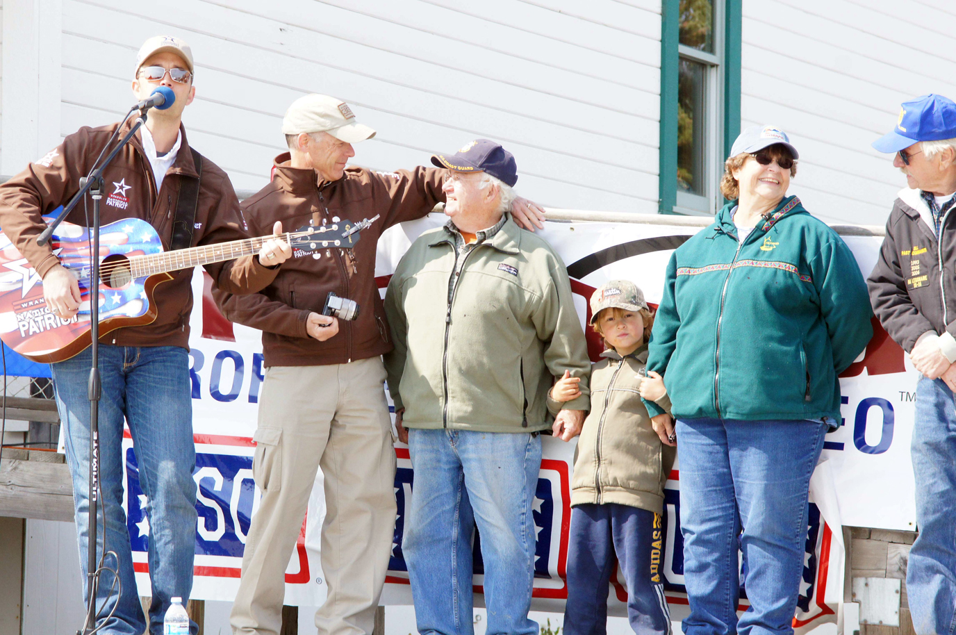 Nashville singer Lucas Hoge, left, performs during the American 300’s presentation of the Wrangler National Patriot Memorial Day Tour in the NOMAR parking lot on Sunday. Rob Powers, second from left, of American 300 honors Ben Mitchell, standing with his grandson Willem, wife Kate and Bill Sheldon of American Legion Post 16.  -Photo provided