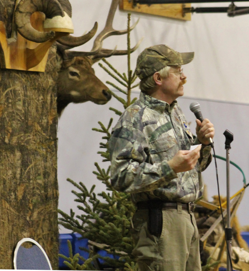 Rick Paulsrud emcees the 2014 Sportsman’s Banquet at Chapman School in Anchor Point, while a taxidermied deer stares over his shoulder.-Photo provided