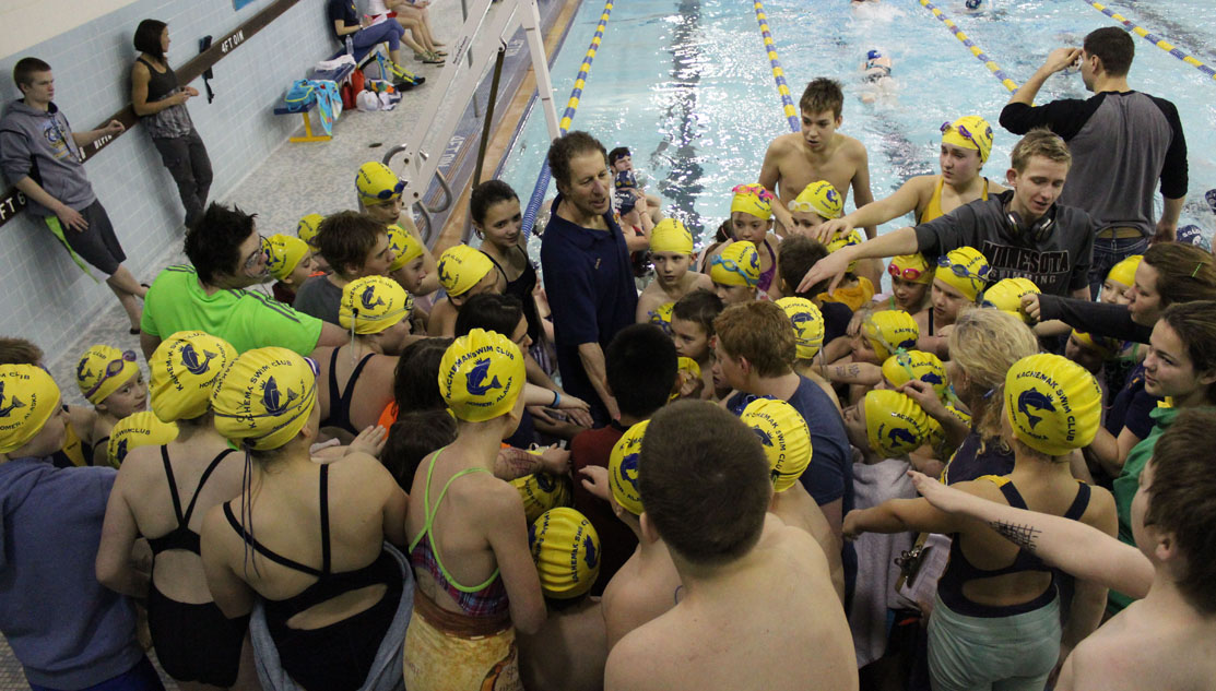 Members of the Kachemak Swim Club gather around the club’s Head Coach, Neil Romney, for a team cheer Saturday morning, the second day of the 2015 End of the Road meet at the Kate Kuhns Aquatic Center.-Photo by McKibben Jackinsky, Homer News