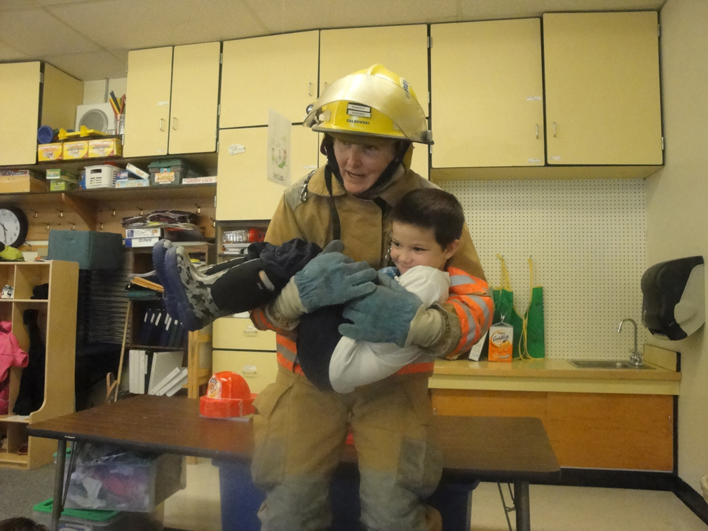 Firefighter Elaine Grabowski demonstrates a “fireman’s carry” with 4-year-old Georgie Farren during a fire safety lesson at Paul Banks Elementary School.   -Photo by Emily Priest