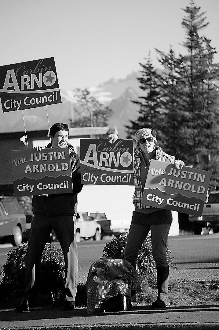 Josh Garvey, left, and Elizabeth Garvey wave signs for Corbin Arno and Justin Arnold during the evening rush hour on Pioneer Avenue on Tuesday.-Photo by Michael Armstrong, Homer News