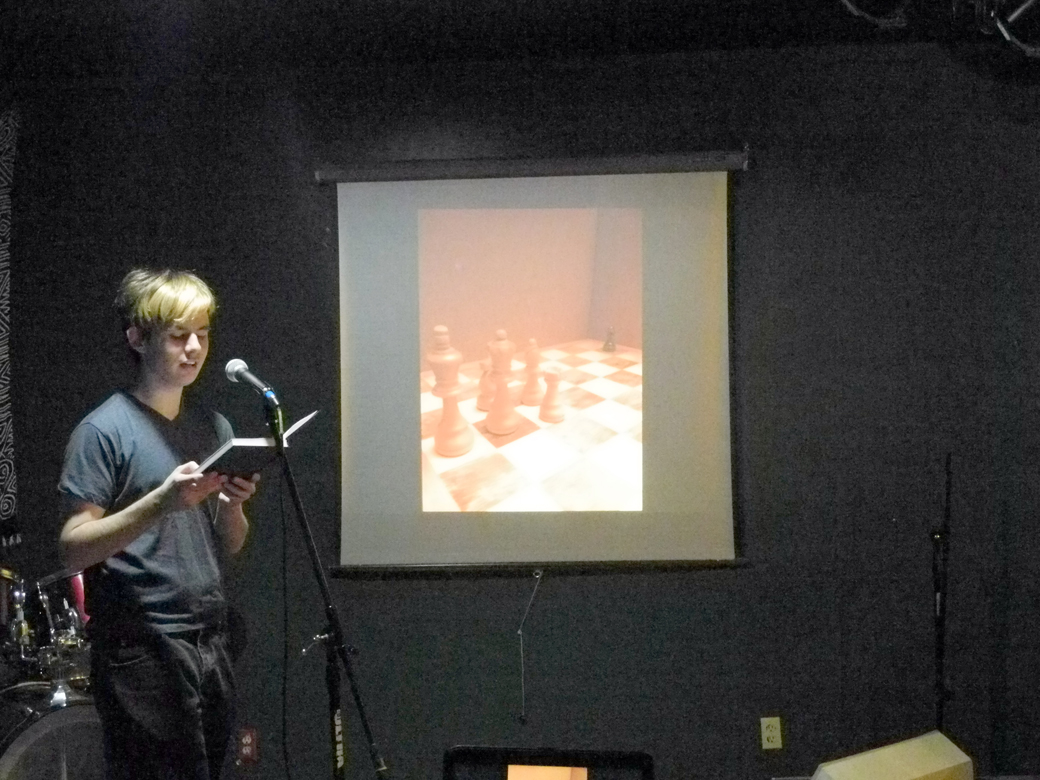 Matthew Myer reads a poem he wrote inspired by Douglas Dean’s photo, “The Forgotten Piece,” shown projected next to him, at the First Friday opening of the PhotoVoice exhibit.-Photo by Michael Armstrong, Homer News