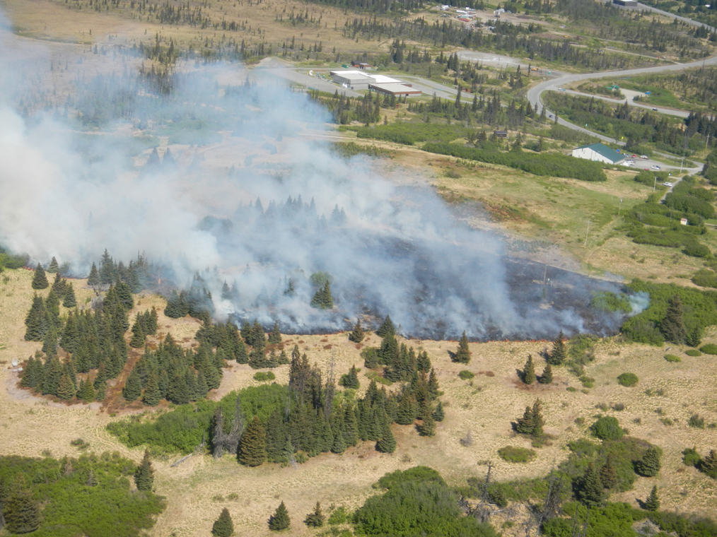 This aerial photo of the Sandra Street fire shows flames burning through grass just west of the Kachemak Emergency Services McNeil Canyon Fire Station, right, and McNeil Canyon Elementary School, center.                              -Photo by Alaska Division of Forestry