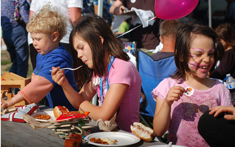 Audrey Dabney, center, and Keeley Dabney, right, eat at the Governor’s Family Picnic last Thursday.-Photo by Michael Armstrong, Homer News