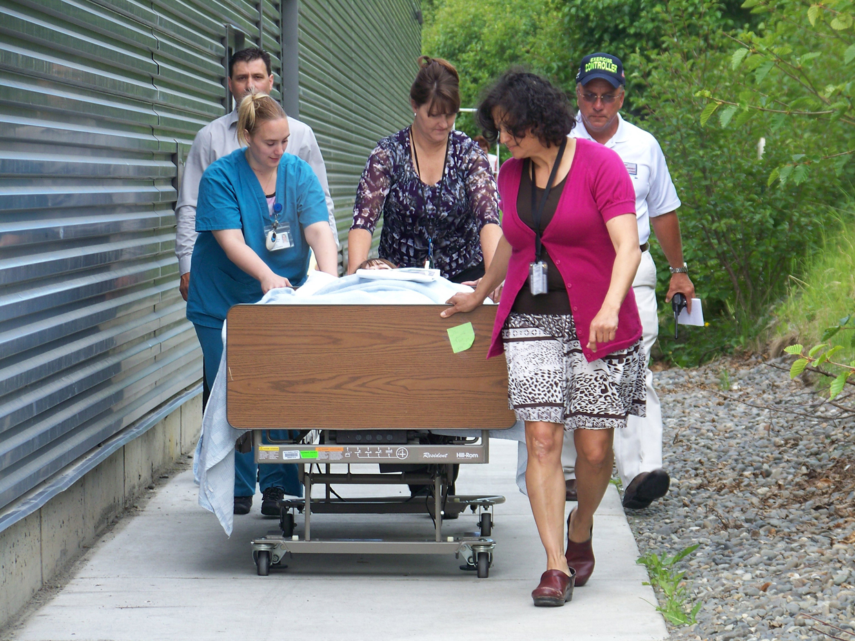 During an evacuation drill at South Peninsula Hospital on Tuesday, a non-ambulatory patient, role-played by Lindsey Yates, is evacuated by hospital staff Martha Roderick, Kelly Luck and Jessie Cashman. In back, Sheridan Bishop of SPH, left, and Bob Becker of Incident Management Solutions, observe.-Photos by McKibben Jackinsky, Homer News