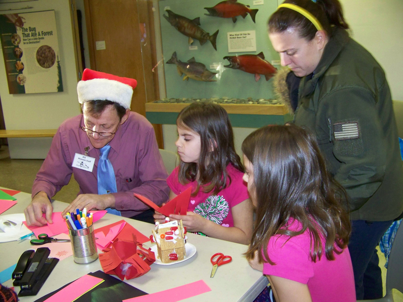 Bill Walker, exhibits assistant of the Pratt Museum, gives Paige and Morgan Haines, 8, of Homer some craft tips at the museum’s Stocking Stuffer Party on Saturday.-McKibben Jackinsky,  Homer News