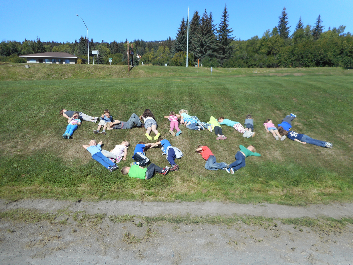 Students in Wendy Todd’s first-grade class at Paul Banks Elementary School use their bodies to spell out “thank you” after a visit to the Kenai Peninsula Fair in Ninilchik. The students wrote the following thank-you letter: Thank you for letting us go to the fair.  We liked the Legos and ribbons that 4H club showed us.  We loved seeing the animals, especially petting the alligator and visiting the parrot.  The picnic with the cool music was awesome.  Thank you for letting us make the candles out of beeswax. We especially enjoyed the pig races. We really loved everything we did there, including the cotton candy you gave us! Thank you again for inviting us.-A big thank you for fair fun