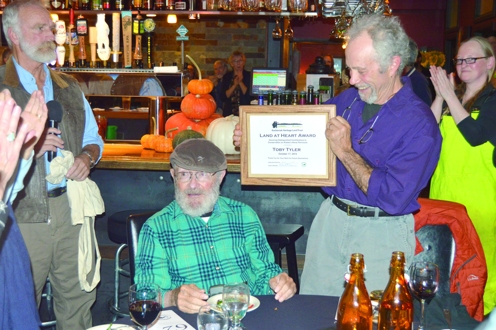 Toby Tyler accepts applause as Dale Chorman holds up Tyler’s award at the Kachemak Heritage Land Trust’s annual auction Saturday night at Wasabi’s.-Annie Rosenthal, Homer News