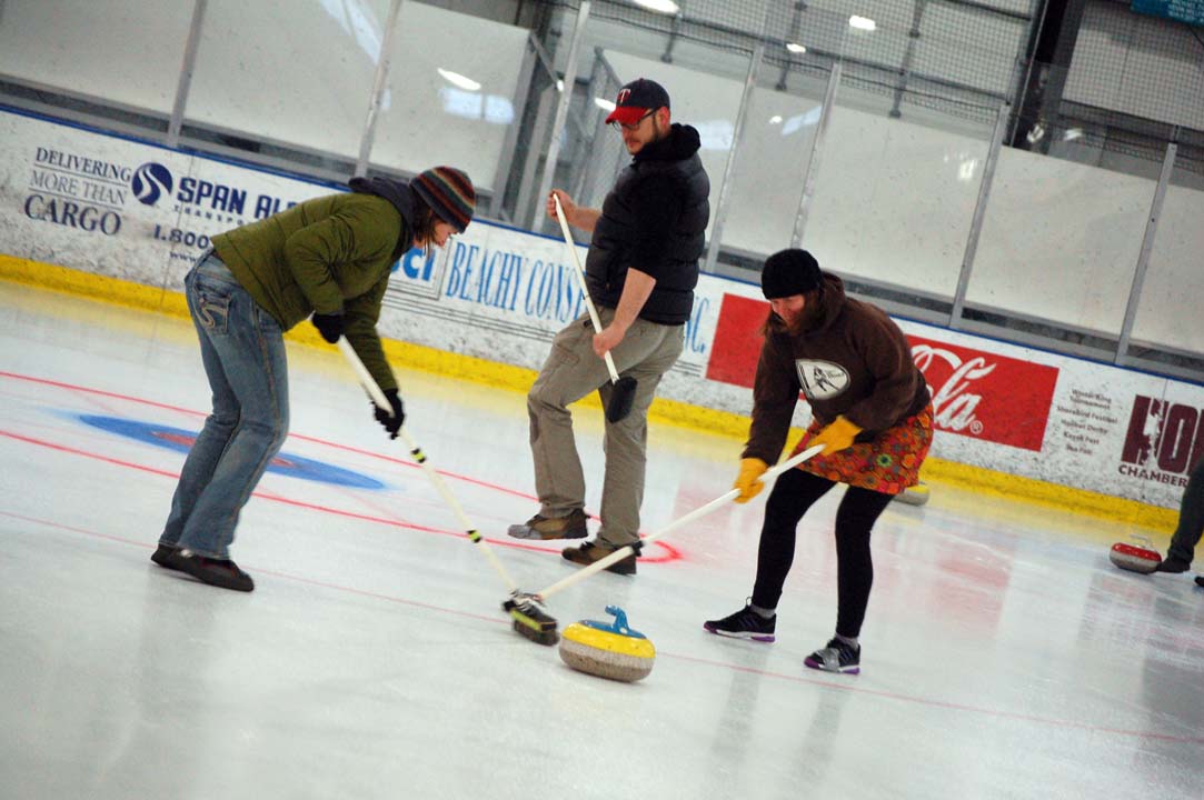 From left to right, Catriona Lowe, Joel Vos and Karen Noyes sweep in front of the stone during  a curling demonstration on Sunday for the Homer Hockey Association’s Kevin Bell Appreciation Day. -Michael Armstrong-Homer News