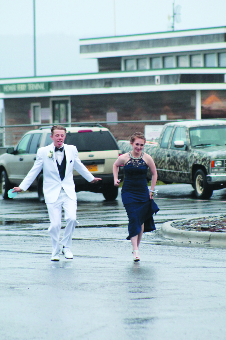 Garrett Butcher and Samantha Jacobsen run through the rain last Saturday at Land’s End Resort for the Homer High School prom. White suits for young men were particularly fashionable at prom this year.-Photo by Anna Frost, Homer News