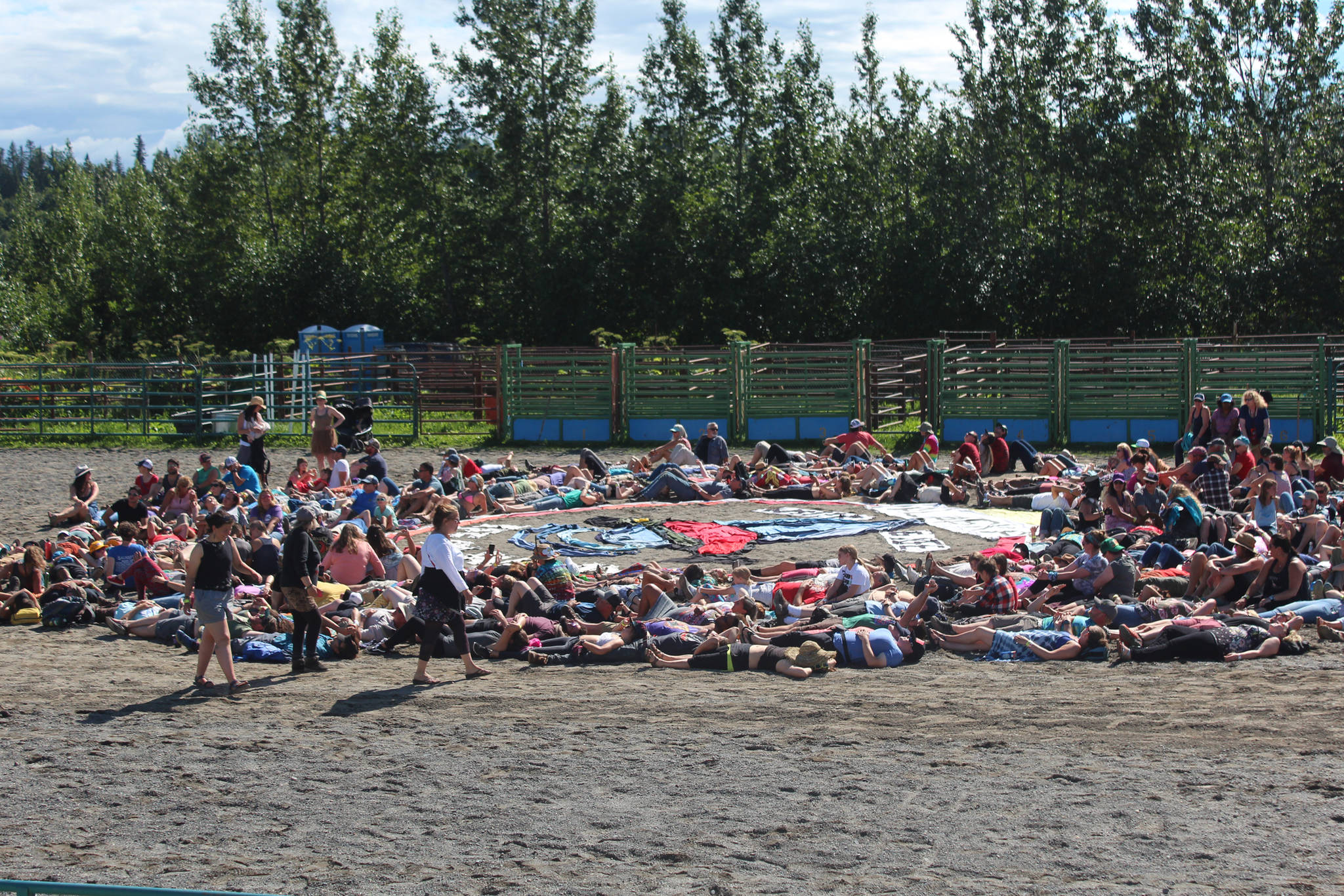 Volunteers and festival goers take their places on the ground to be part of this year’s art installation at Salmonfest on Saturday, Aug. 4, 2018 in Ninilchik, Alaska. Coordinated each year by Homer artist Mavis Muller, the project is a human and fabric mosaic piece which always includes a message about the importance of salmon and water. The installation is completed by being photographed from above by a drone. (Photo by Megan Pacer/Homer News)