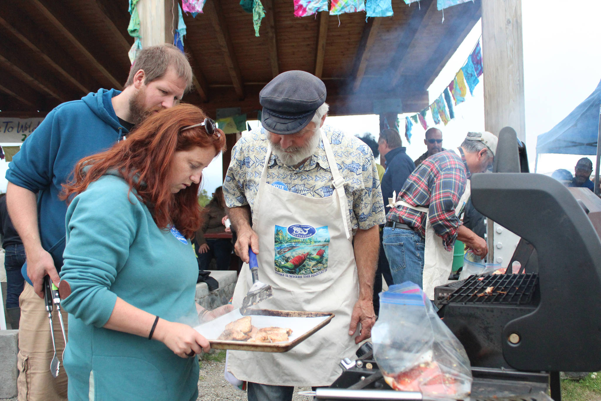 Alaska Rep. Paul Seaton (right) grills salmon with the help of his son, Rand, (left) and daughter-in-law, Lauren during a barbecue at Karen Hornaday Park for Alaska Wild Salmon Day on Friday, Aug. 10, 2018 in Homer, Alaska. (Photo by Megan Pacer/Homer News)