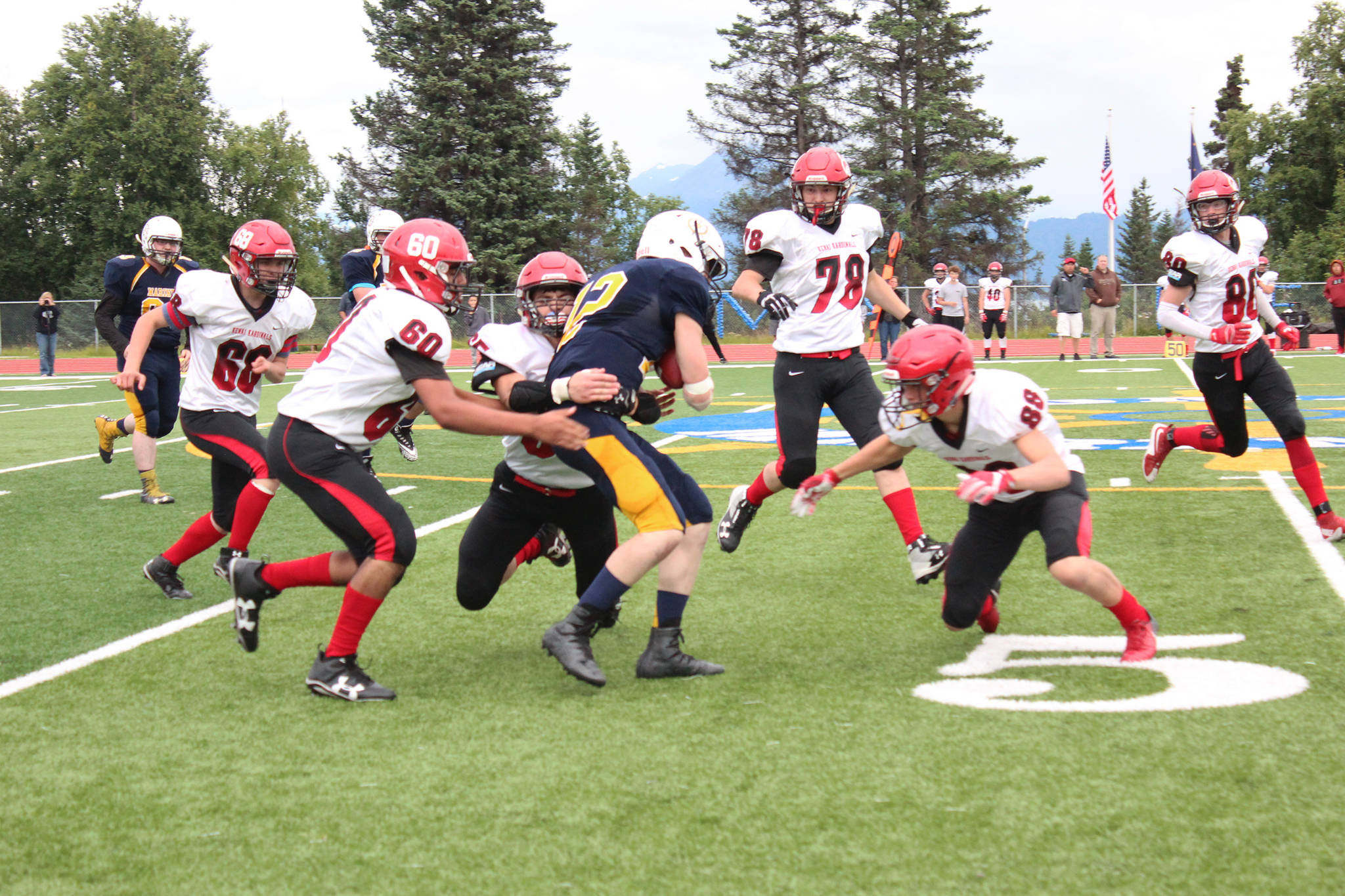 A group of Kardinal football players descend on Homer High School quarterback Anthony Kalugin during their game Friday, Aug. 17, 2018 at the high school in Homer, Alaska. Kenai Central High School beat the Mariners 58-6. (Photo by Megan Pacer/Homer News)