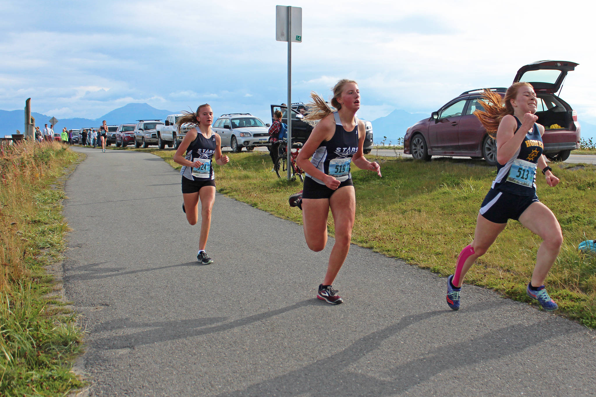 Homer’s Sienna Carey rushes to pass two Soldotna High School cross-country runners at the finish line of the girls 5K race Friday, Sept. 7, 2018 during the Homer Invitational held on the Homer Spit in Homer, Alaska. (Photo by Megan Pacer/Homer News)