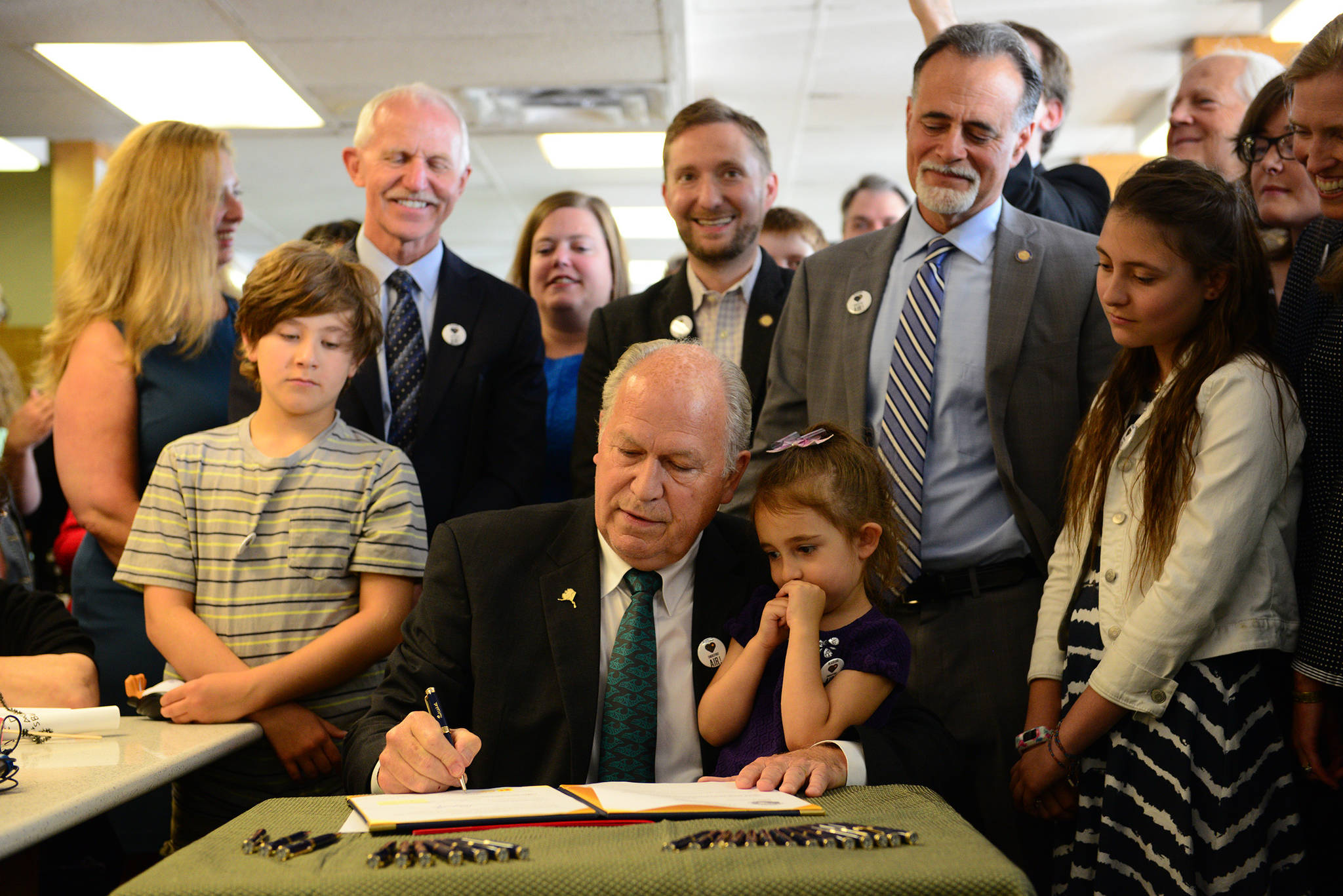 In a photo provided by the office of the governor, Gov. Bill Walker signs Senate Bill 63, a statewide public smoking ban, on Tuesday, July 17, 2018, at the Lucky Wishbone restaurant in Anchorage. The law goes into effect on Oct. 1. Standing at right is Sen. Peter Micciche, R-Soldotna, the legislative sponsor of the bill. On Walker’s lap is Stella Micciche, one of Micciche’s daughters. Also visible, from right to left behind Walker are Dr. Jay Butler, Alaska’s chief medical officer; Rep. Geran Tarr, D-Anchorage; Rep. Jason Grenn, I-Anchorage; Micciche; Rep. Chris Birch, R-Anchorage; and the smile of Emily Nenon of the American Cancer Society. (Courtesy photo)