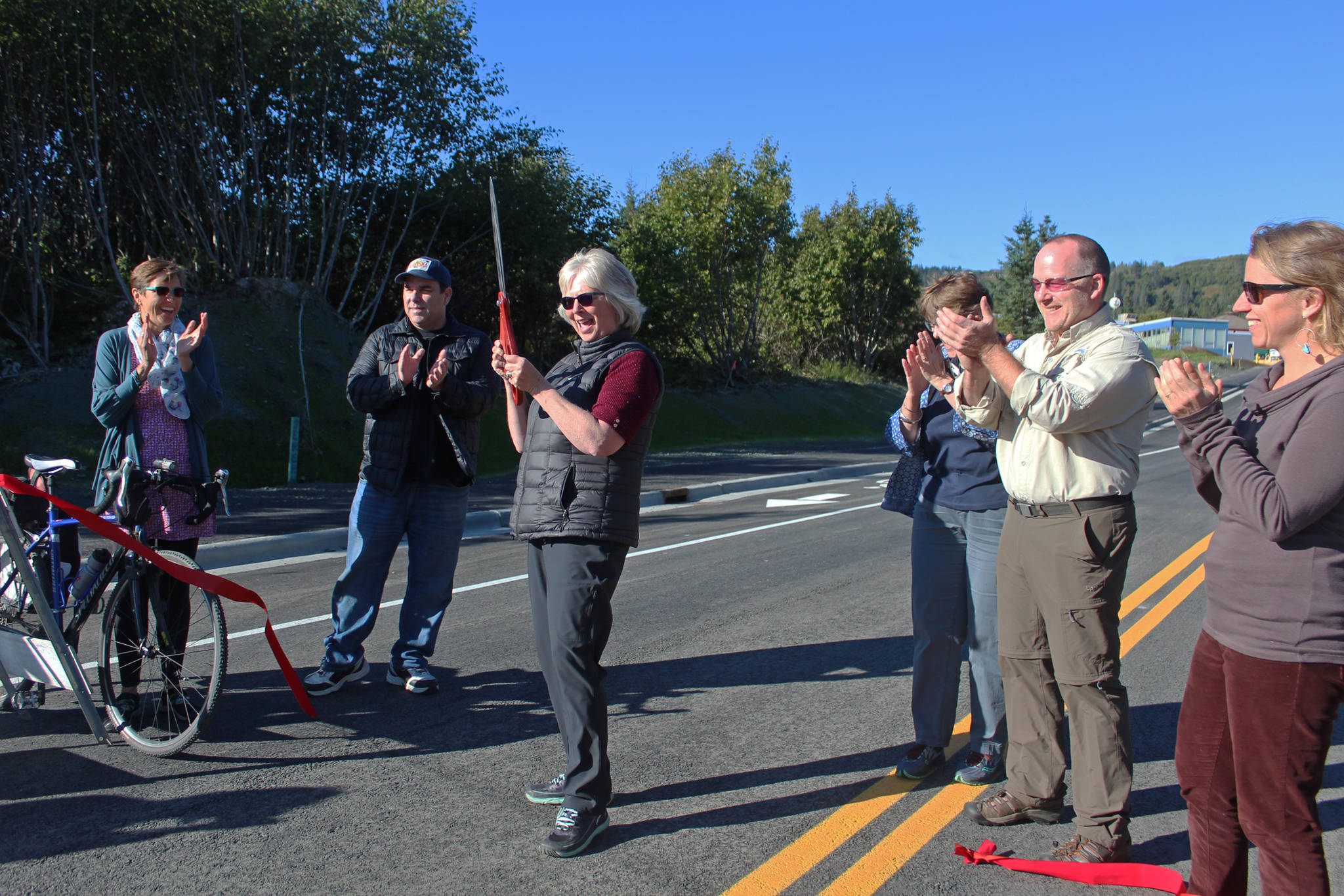 Members of the Homer City Council and Save-U-More Assistant Manager Brian Nahmis (second from left) celebrate after council member Shelly Erickson (third from left) cuts a ribbon in a grand opening ceremony for the completed Greatland Street on Tuesday, Sept. 25, 2018 in Homer, Alaska. (Photo by Megan Pacer/Homer News)