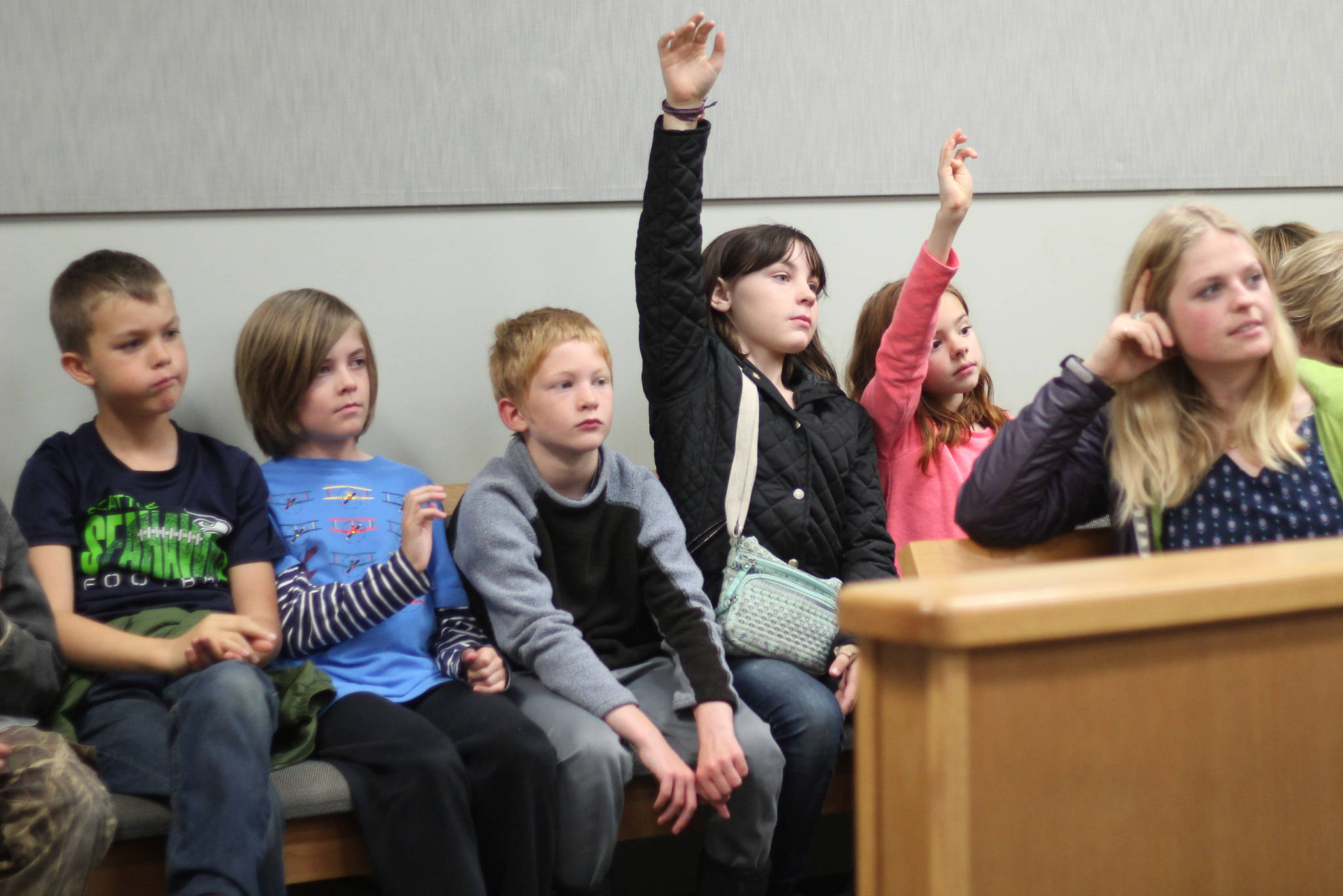 Grace Berumen and Madelyn Madrid raise their hands to ask questions during an Oct. 8, 2018 field trip to the Homer Courthouse in Homer, Alaska. They and their fellow Fireweed Academy classmates learned about the law and the inn workings of the courthouse. (Photo by Megan Pacer/Homer News)