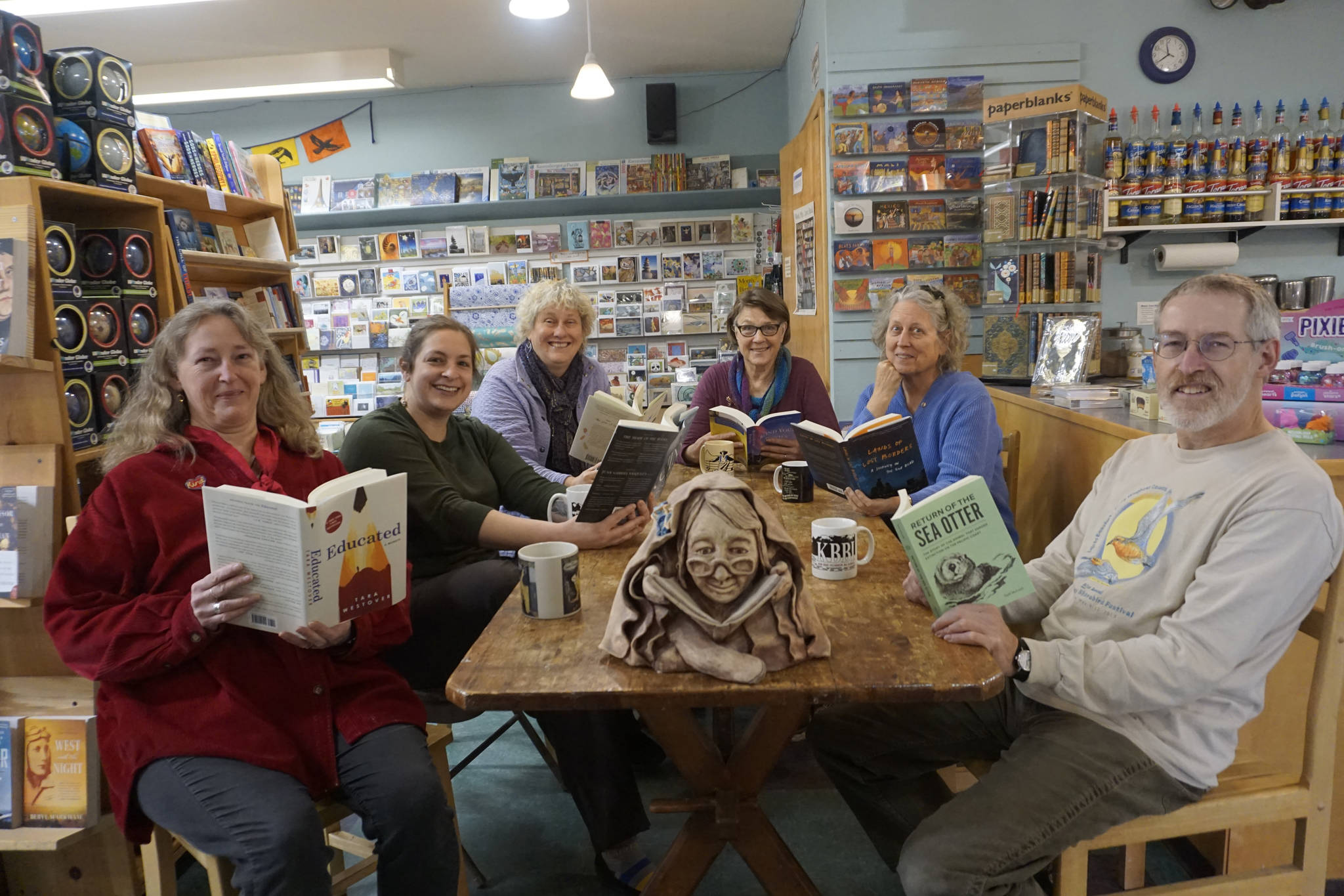 The staff and partners in the Homer Bookstore pose for a photo in the store’s cafe in Homer, Alaska, on Oct. 29, 2018. From left to right are Sue Post, partner; Jennifer Norton, staff; Jennifer Stroyeck, partner; Nancy Vait, staff; Sara Reinert, staff; and Lee Post, partner. The sculpture on the table is of bookstore matriarch Joy Post, mother of Sue and Lee Post, and was sculpted by artist Barbara Jo Auburn House. (Photo by Michael Armstrong/Homer News)