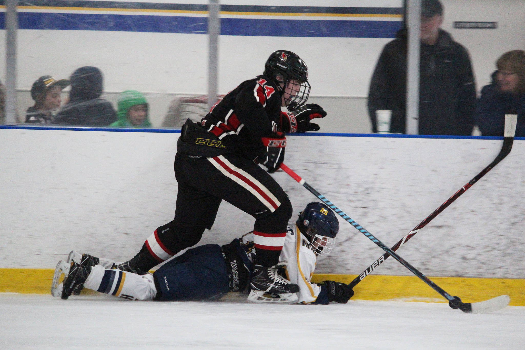 Kenai’s Miles Marsten steps over Homer’s Lee Lowe after Lowe fell while both were chasing the puck during a game between the two schools Friday, Nov. 16, 2018 at the End of the Road Shootout at Kevin Bell Arena in Homer, Alaska. (Photo by Megan Pacer/Homer News)
