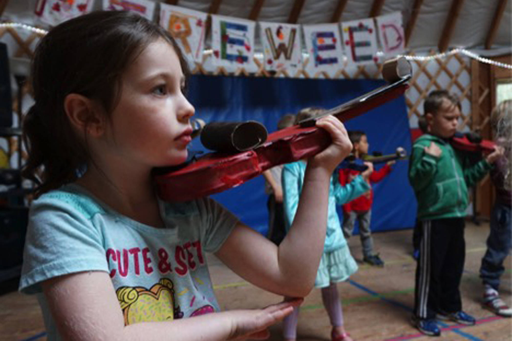 First grade student Elizabeth Parke practices holding a cardboard violin, in anticipation of the real thing, at Fireweed Academy in Homer, Alaska. (Photo by Miranda Weiss)