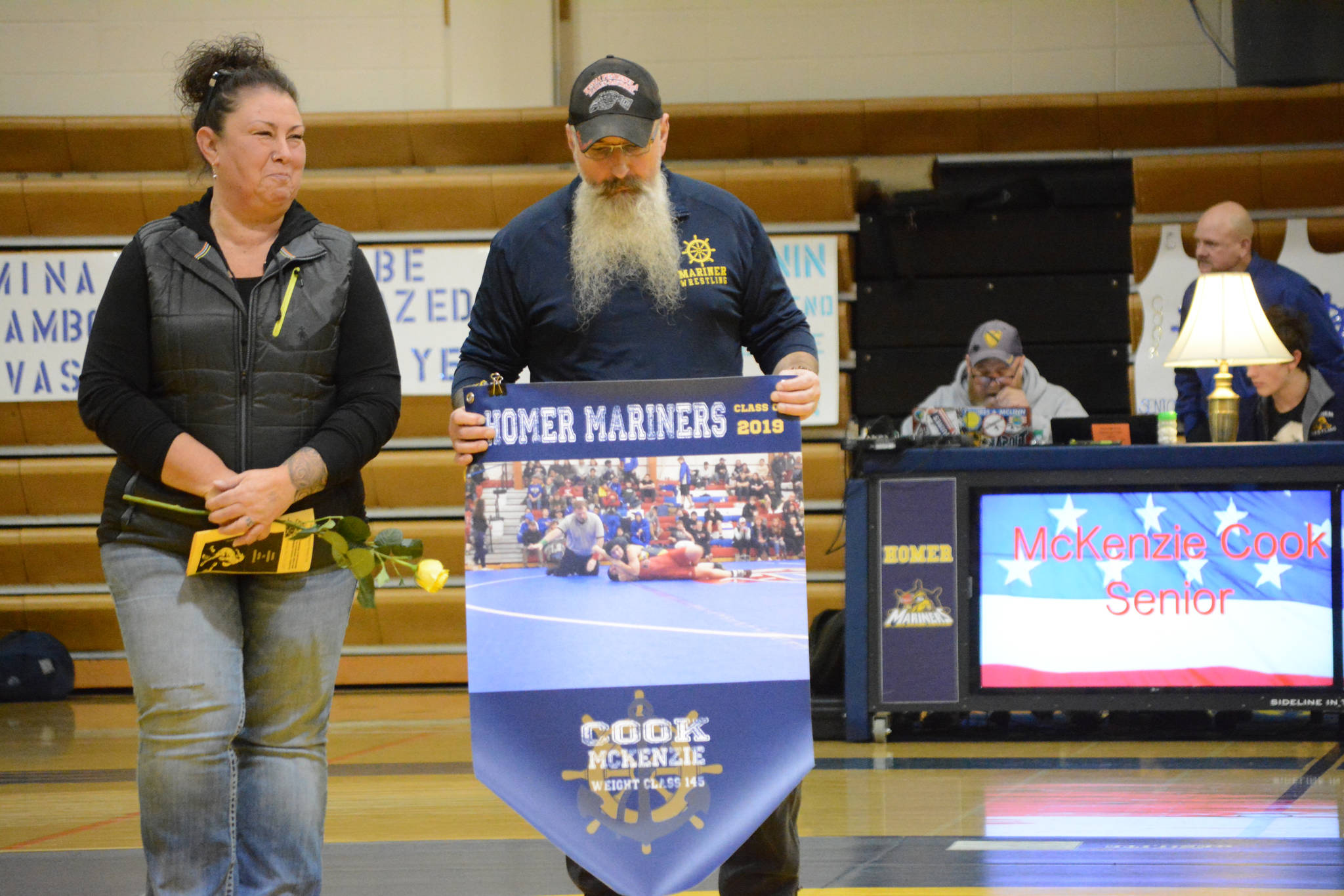 Tammie Cook, left, and Todd Cook, right, holds a banner recognizing their daughter, McKenzie Cook, at Senior Night, the Homer-Kenai dual wrestling meet held Nov. 21, 2018, in the Homer High School Alice Witte Gym, Homer, Alaska. (Photo by Michael Armstrong/Homer News)