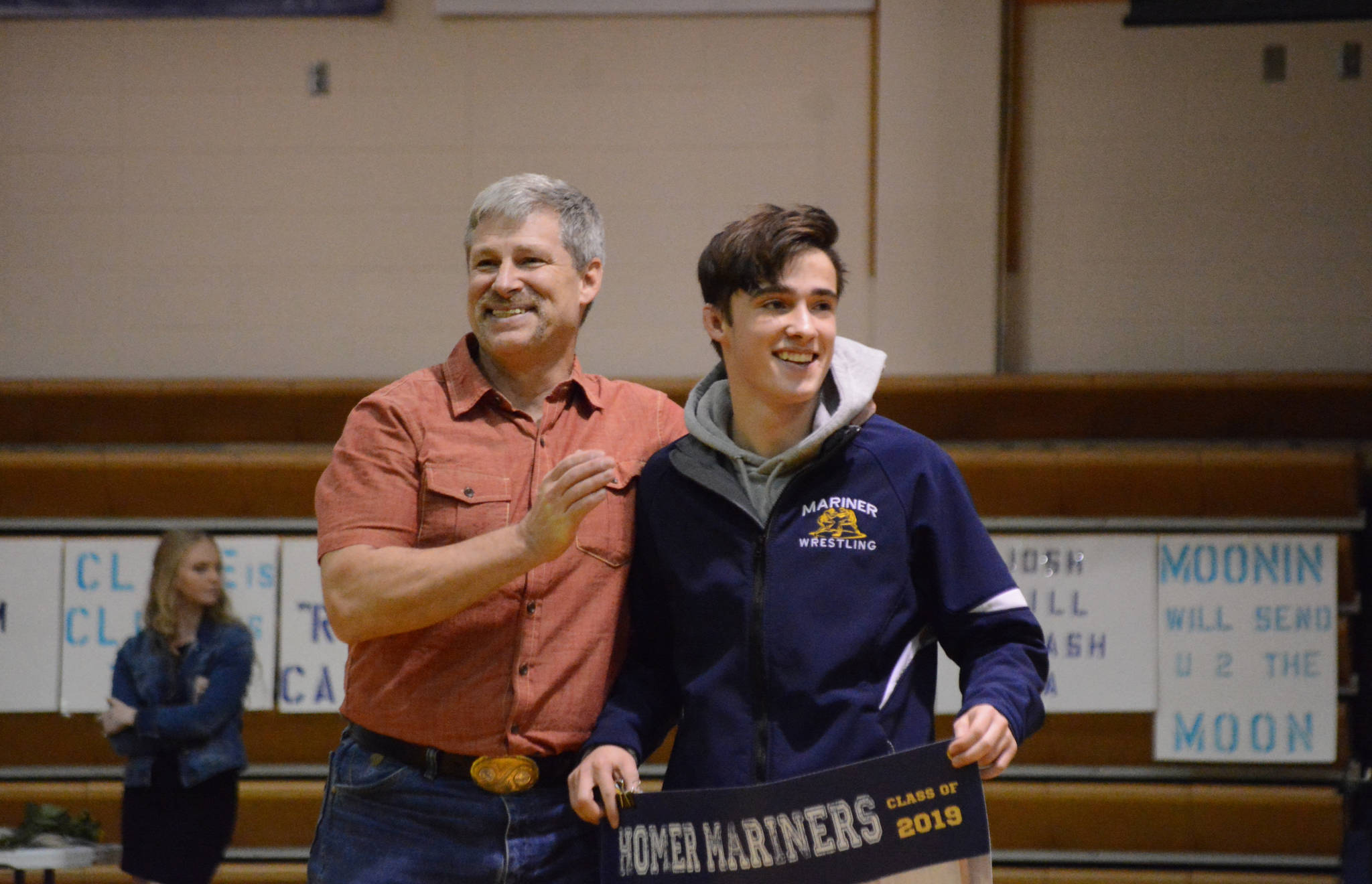 Seth Inama holds a banner recognizing him at Senior Night, the Homer-Kenai dual wrestling meet held Nov. 21, 2018, in the Homer High School Alice Witte Gym, Homer, Alaska. Supporting him is his father, Jay Inama. (Photo by Michael Armstrong/Homer News)