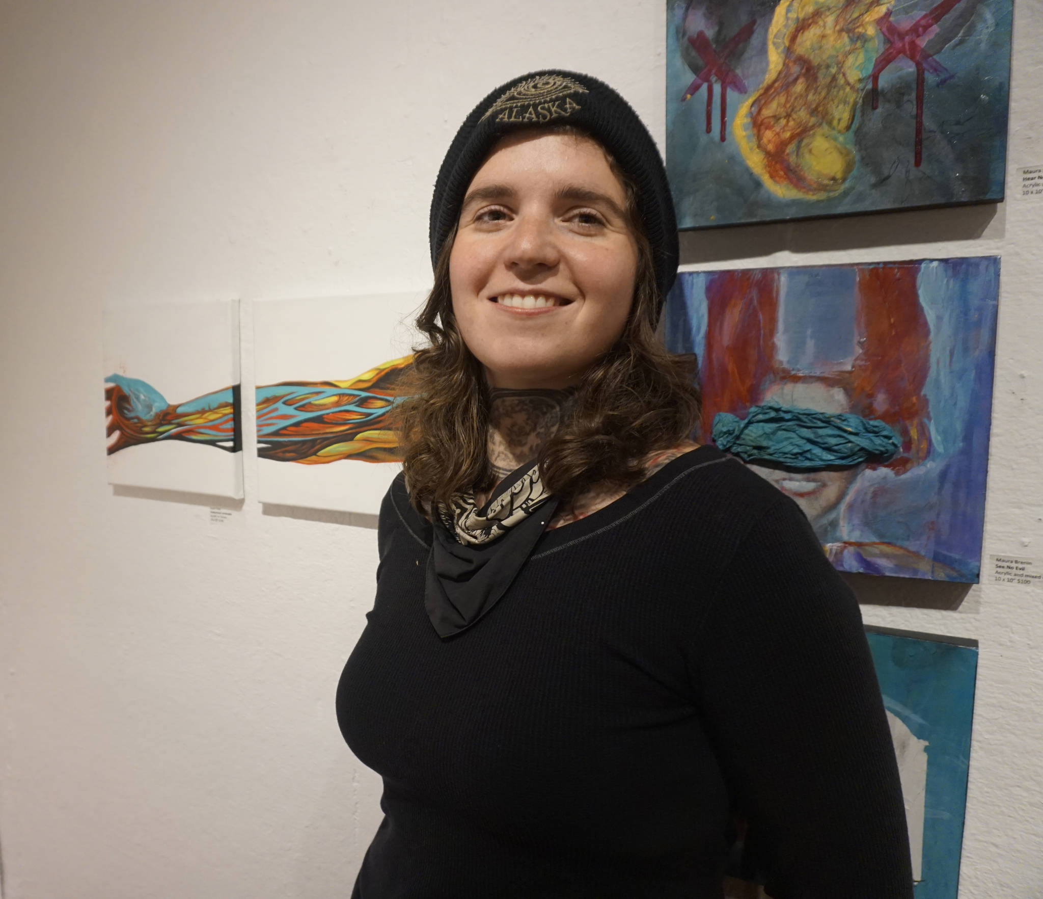 Sarah Frary stands by her paintings, “Anatomical Landscape,” left, at the First Friday, Dec 7, 2018, opening of Bunnell Street Arts Center’s 10x10 show in Homer, Alaska. (Photo by Michael Armstrong/ Homer News)