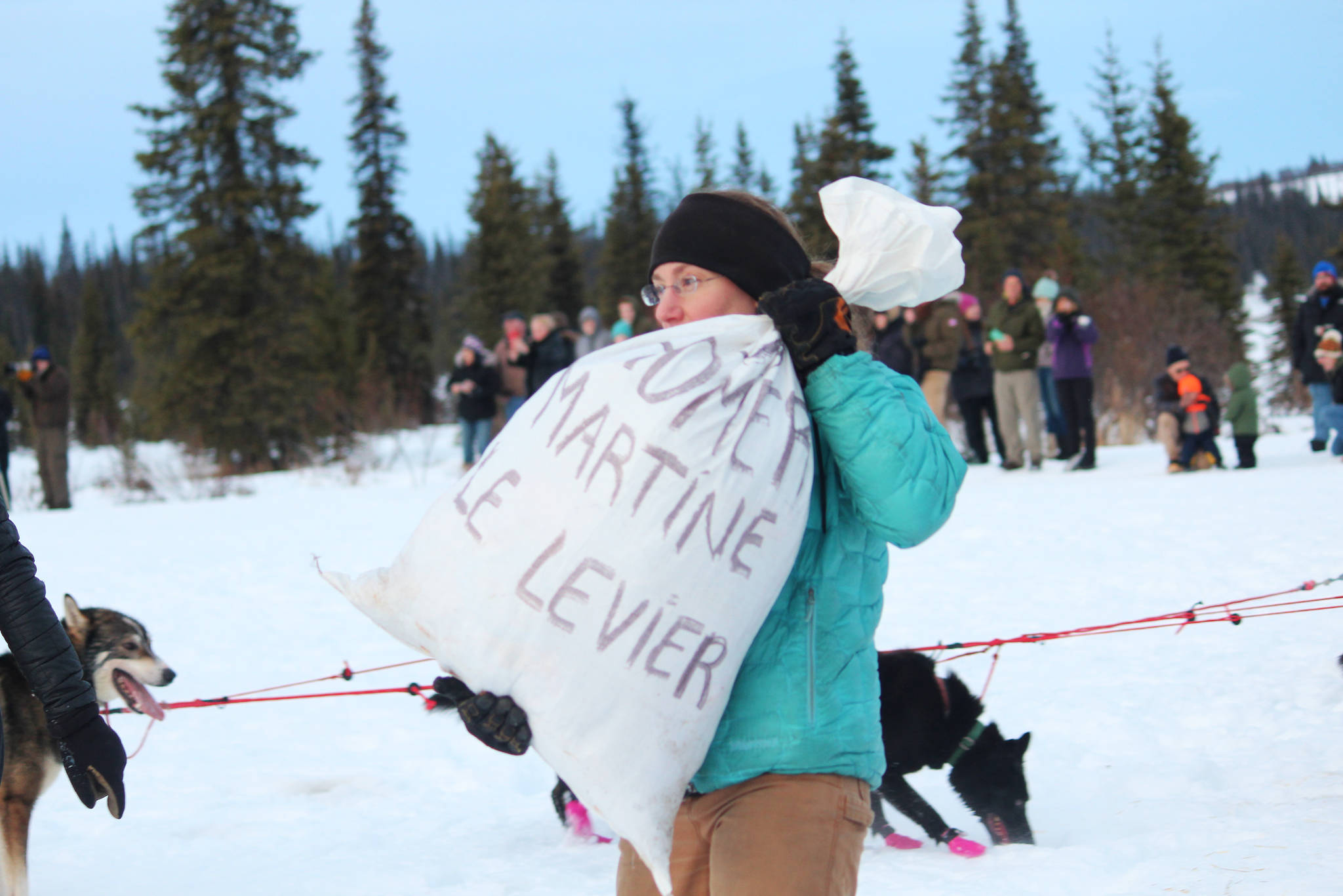 A volunteer carries a bag of supplies to one of the mushers in this year’s Tustumena 200 Sled Dog Race while at the first checkpoint Saturday, Jan. 26, 2019 at McNeil Canyon Elementary School near Homer, Alaska. (Photo by Megan Pacer/Homer News)