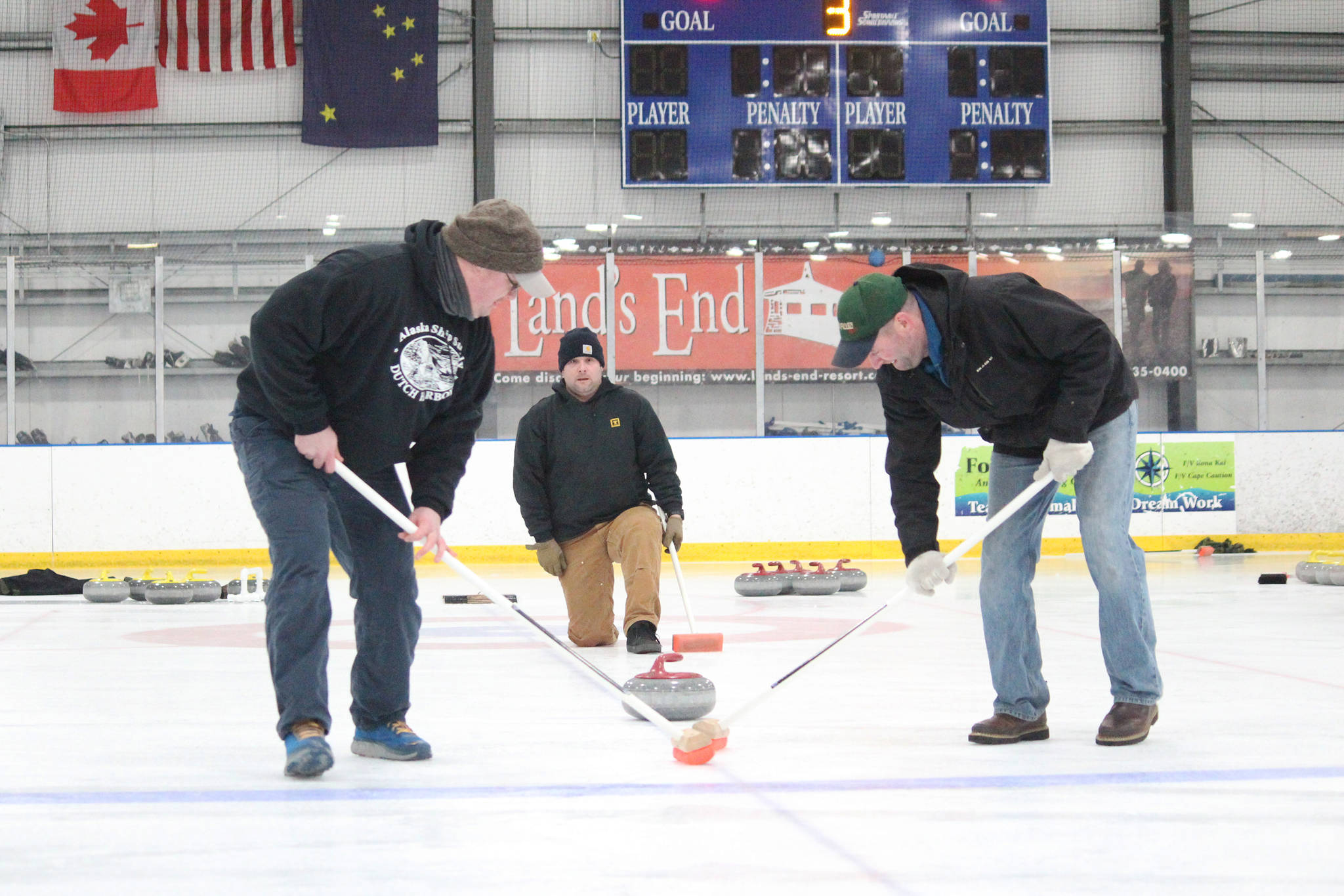 Mike Kozloski (left), Chuck Bowman (center) and Steve Nelzen work together to deliver and sweep a curling stone during a Learn to Curl fundraiser event for the Homer Curling Club on Saturday, Jan. 12, 2019 at the Kevin Bell Arena in Homer, Alaska. The clinic was taught by former Olympic curler Jessica Schultz. (Photo by Megan Pacer/Homer News)