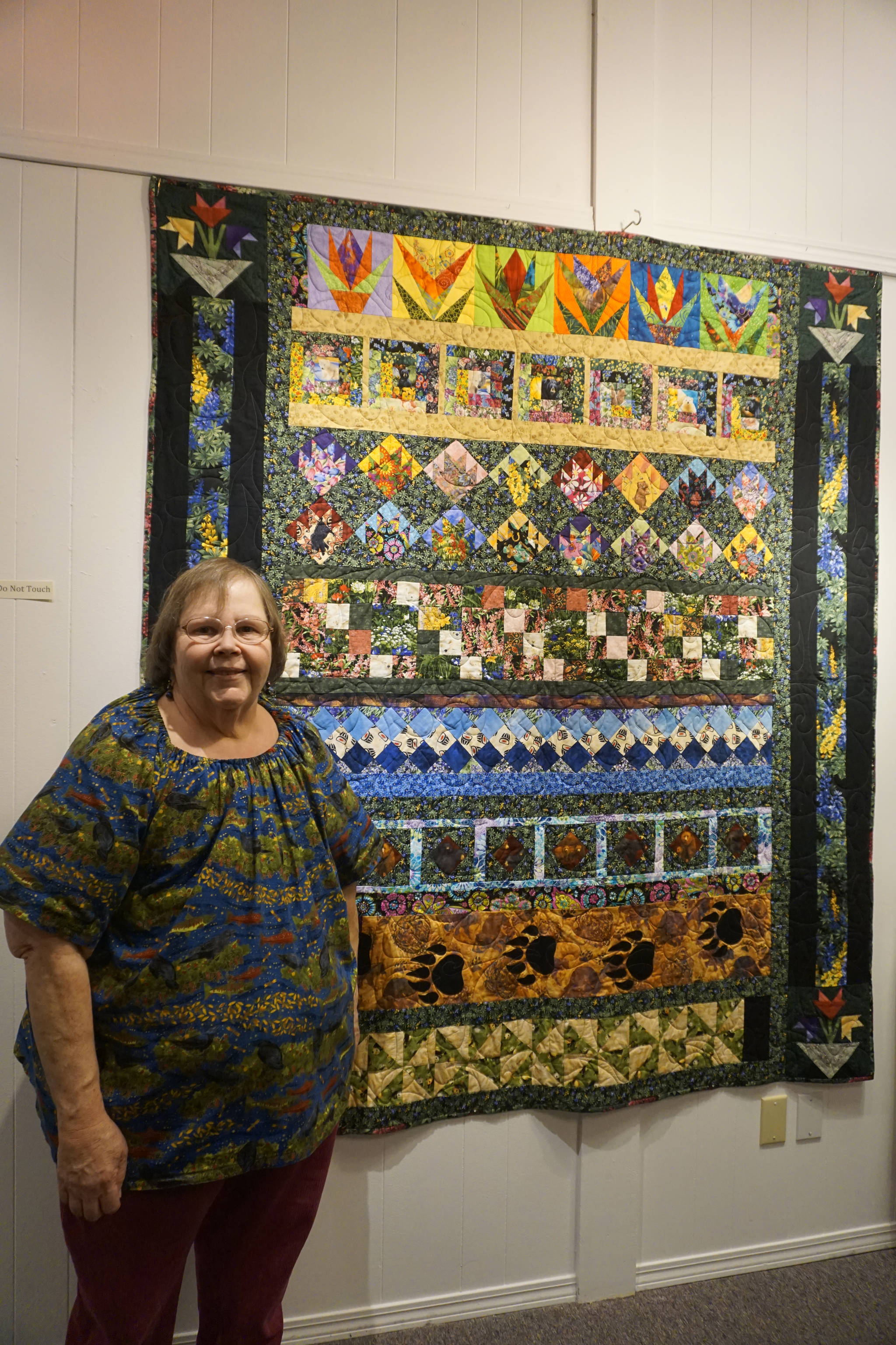 Linda Wagner stands by her “Bears and Flowers” quilt, quilt, one of the works in the “9 Women / 9 Quilts” show that opened last Friday, Feb. 1, 2019, at the Homer Council on the Arts, in Homer, Alaska. (Photo by Michael Armstrong/Homer News)