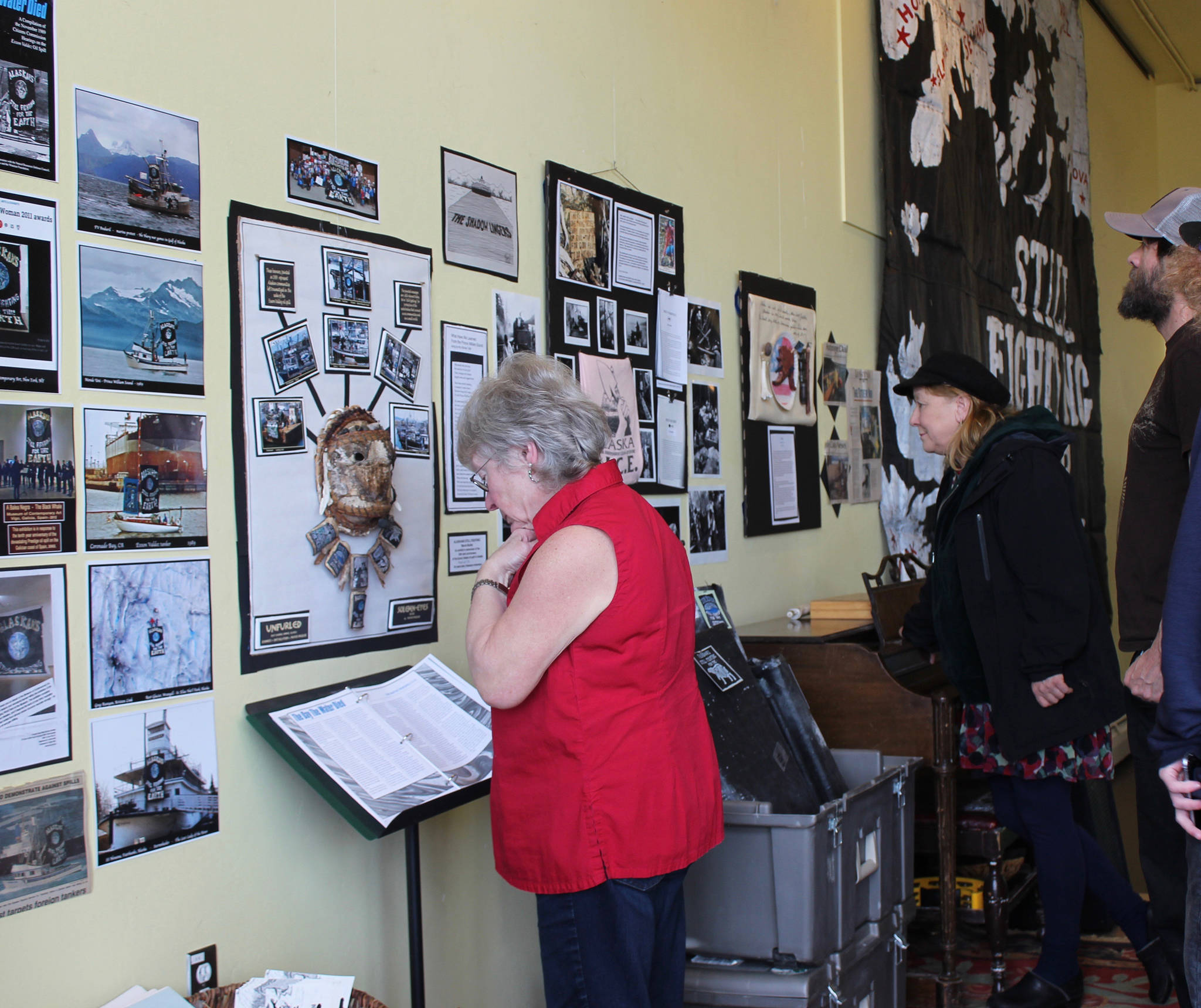 Roberta Highland, Sue Christiansen, and Jason Weir examine “spill-mobelia” included in “Still Fighting,” an exhibit by Homer artivist Mavis Muller Saturday, March 23, 2019 on display at KBay Caffe in Homer, Alaska. The exhibit recalls the Exxon Valdez oil spill of March 24, 1989, and the response of locals and visitors to protect wildlife and beaches. (Photo by McKibben Jackinsky)