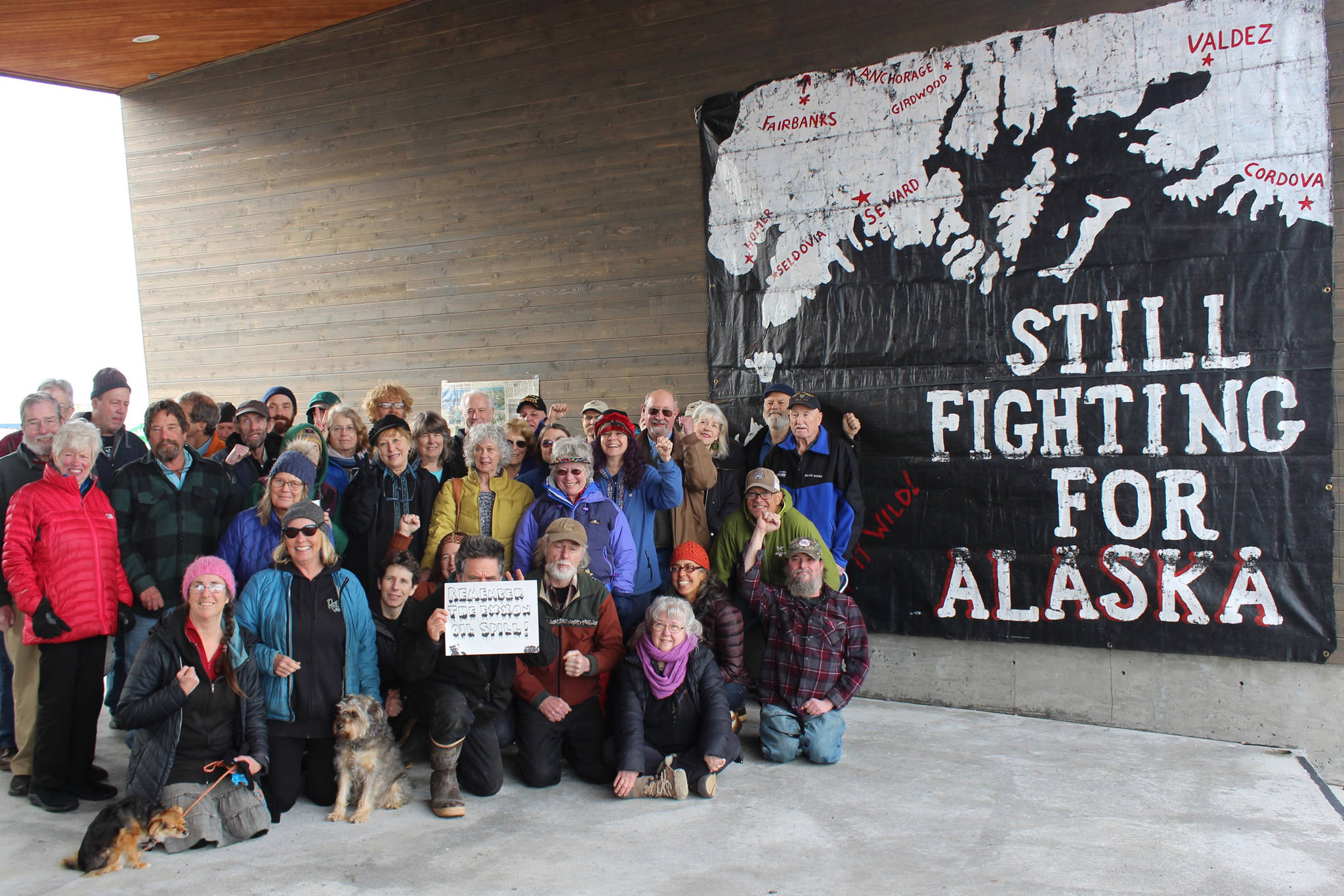 Homer-area residents pose in front of the “Still Fighting for Alaska” banner Homer artivist Mavis Muller made after the March 24, 1989, grounding of the Exxon Valdez, during a gathering on Sunday, March 24, 2019 on the Homer Spit in Homer, Alaska. A tear in the tanker’s hull allowed millions of gallons of Alaska crude to spill into Prince William Sound, fouling more than a thousand miles of Alaska’s coastline. (Photo by McKibben Jackinsky)