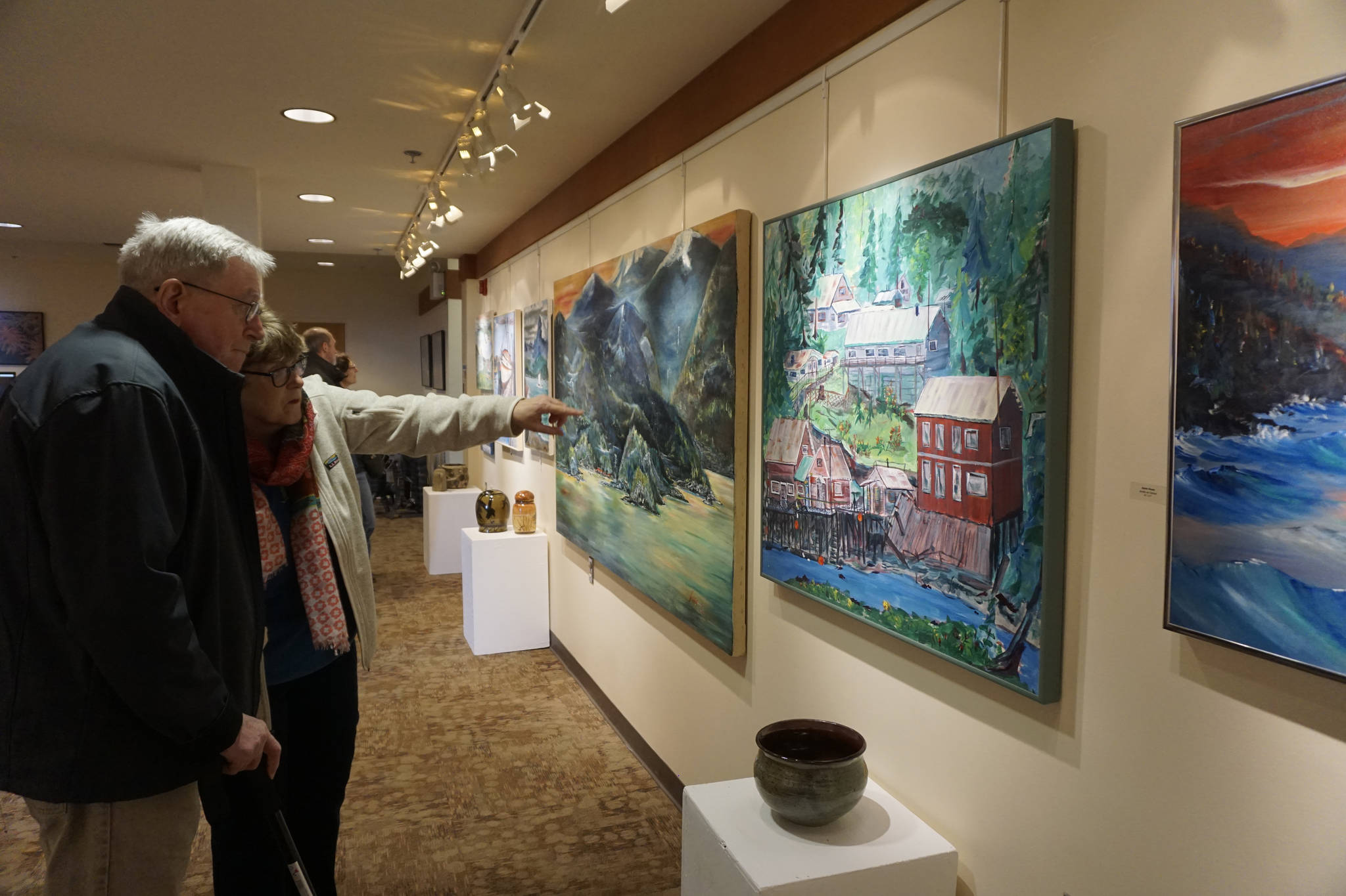 Franco and Caroline Venuti look at John Fenske’s paintings at the First Friday, April 5, 2019, opening for his retrospective showing at Kachemak Bay Campus in Homer, Alaska. (Photo by Michael Armstrong/Homer News)