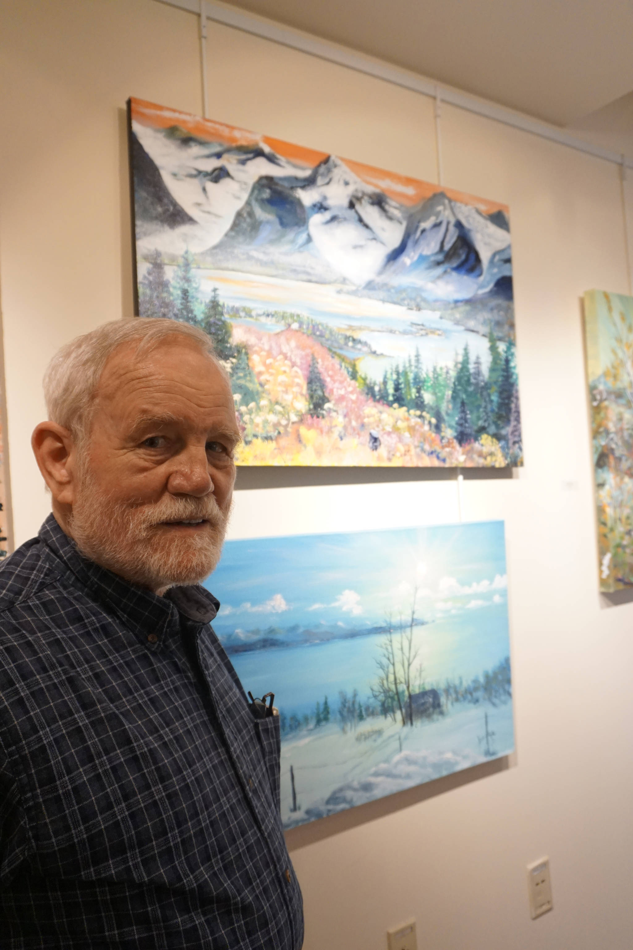 Bill Smith stands by a John Fenske painting, top, that his children bought for him. Fenske’s retrospective show opened on First Friday, April 5, 2019, at Kachemak Bay Campus in Homer, Alaska. (Photo by Michael Armstrong/Homer News)