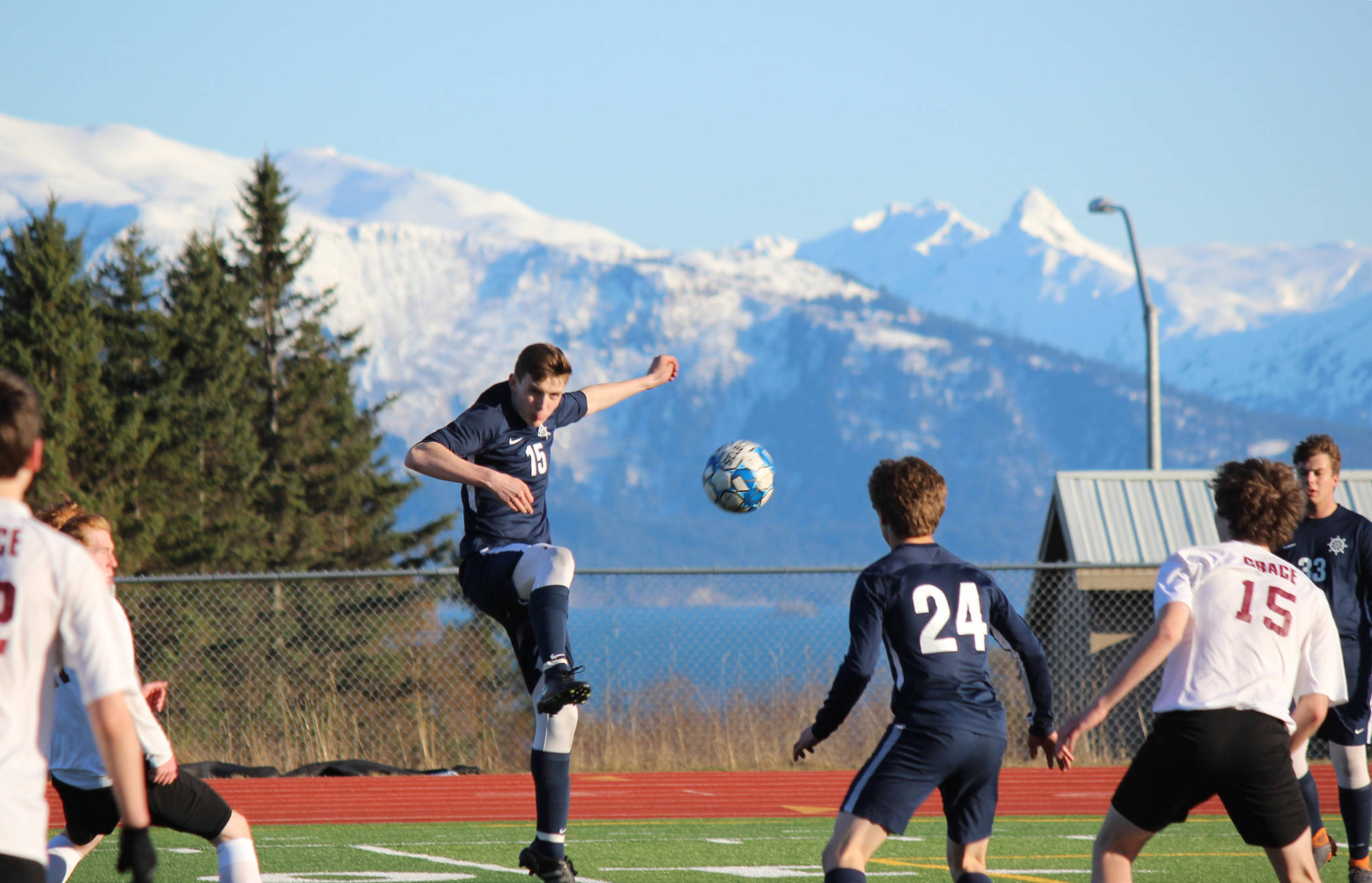 Homer Mariner Ethan Pitzman, 15, keeps the ball in play during Friday’s game against Grace Christian, Friday, April 26, 2019, at the high school in Homer, Alaska while teammates Austin Shafford, 24, and Henry Russell, 33, keep the Grace Christian team at a distance. (Photo by McKibben Jackinsky)