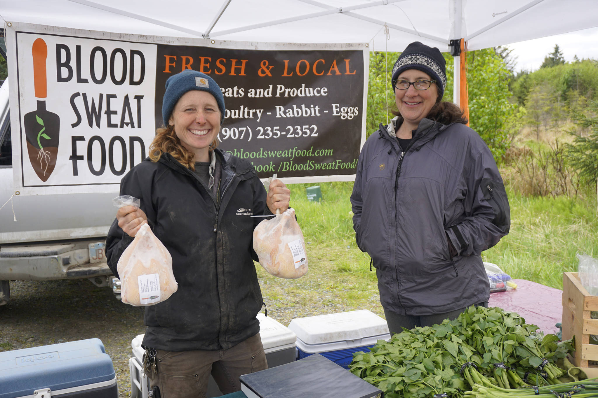 Jenni Medley of Blood, Sweat and Food holds up fresh chickens while Jen Becker watches at the opening of the Homer Farmers Market on May 25, 2019, in Homer, Alaska. (Photo by Michael Armstrong/Homer News)