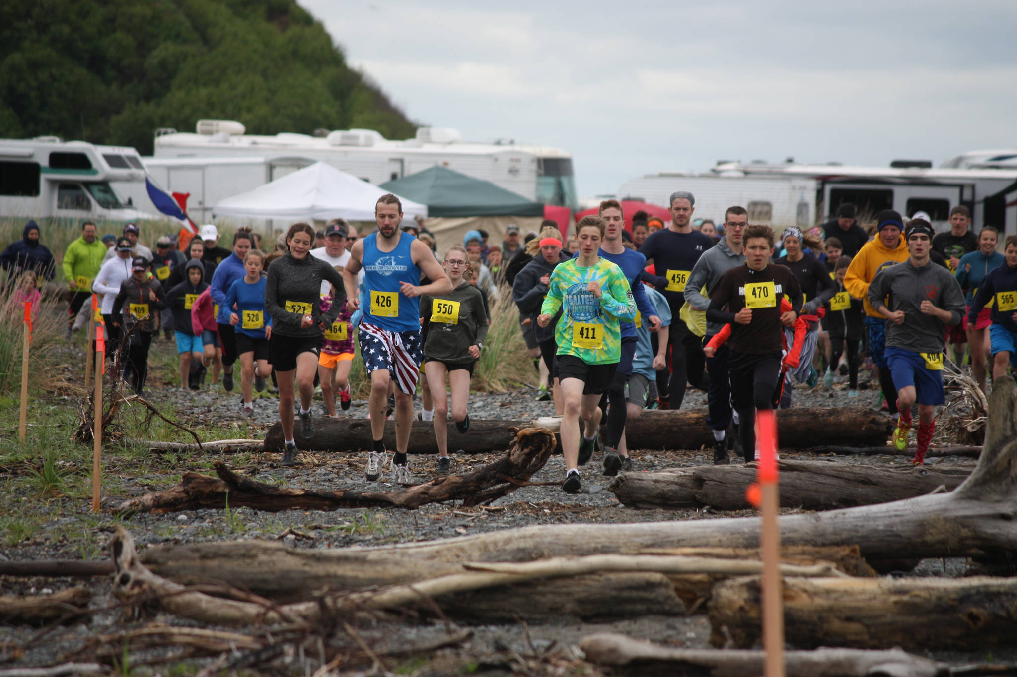Runners in the 2018 Clam Scramble leave the starting line on the south side of Deep Creek and encounter their first obstacle: driftwood logs organizers of the 5K fun run laid across the course. The 2018 5K Clam Scramble was held June 16, 2018, in Ninilchik, Alaska. The fun run is held during low tide on Ninilchik beach. (Photo by Sabrina Ferguson)