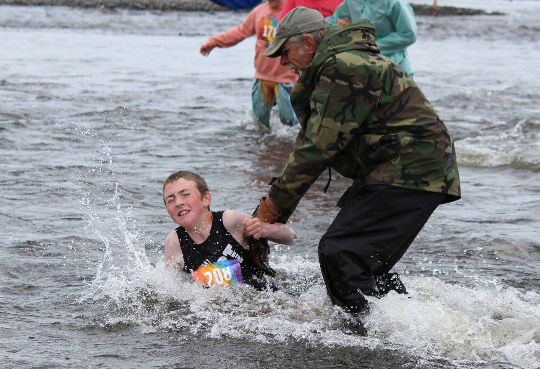 A cold-water stumble doesn’t slow runner Kael Aamodt, 111, thanks to a little help from a race volunteer during the Clam Scramble held Saturday, June 15, 2019 in Ninilchik, Alaska. (Photo by McKibben Jackinsky)