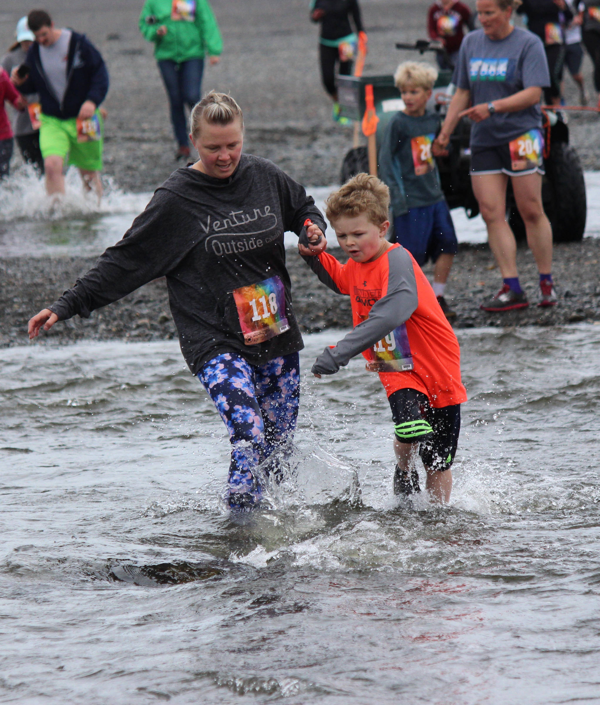 Whitney Schollenberg, 118, and Parker Schollenberg, 119, offer each other a steady hand while crossing the mouth of Deep Creek during the Clam Scramble on Saturday, June 15, 2019 in Ninilchik, Alaska. (Photo by McKibben Jackinsky)