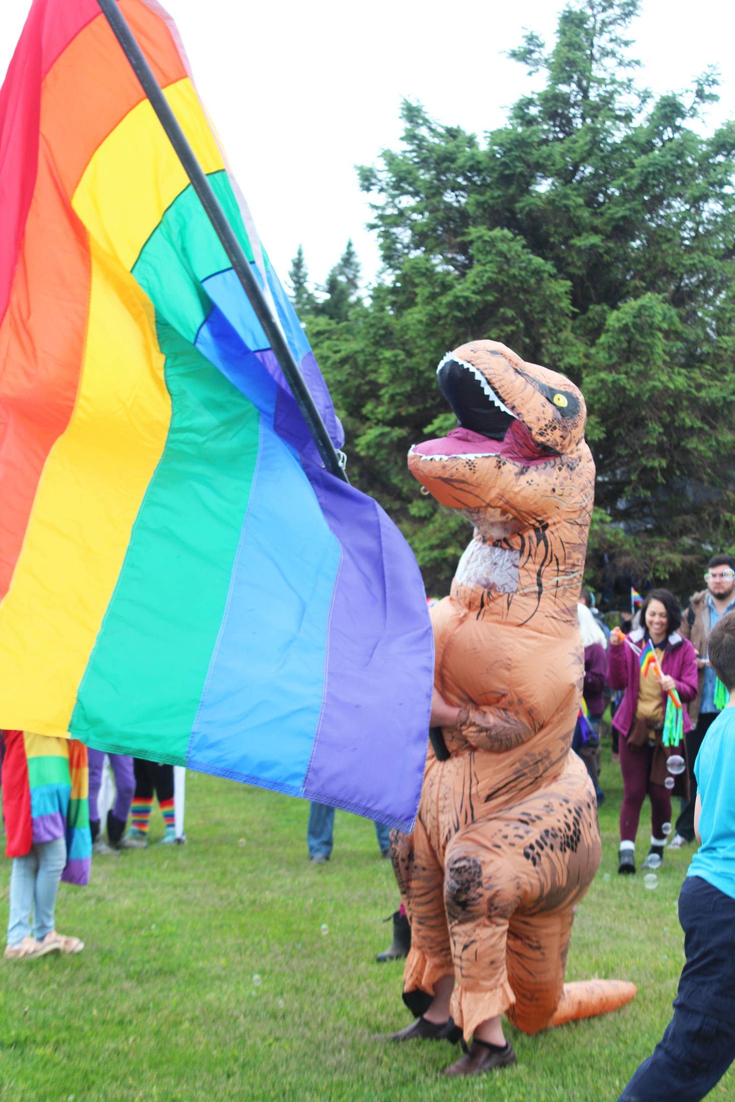 Gage Dillon, 14, waves a pride flag while dressed in a dinosaur suit before Homer’s first ever Pride March on Saturday, June 23, 2018 at WKFL Park in Homer, Alaska. (Photo by Megan Pacer/Homer News)