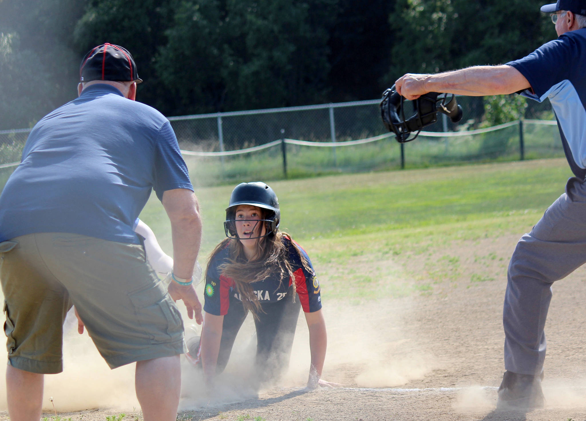 AK Riptide’s Amber Nash land on third base in a cloud of dust with her eyes on Coach Bob Frates on June 29, 2019, at Jack Gist Field in Homer, Alaska. Umpire BIll Bell signals that Nash is safe. (Photo by McKibben Jackinsky)