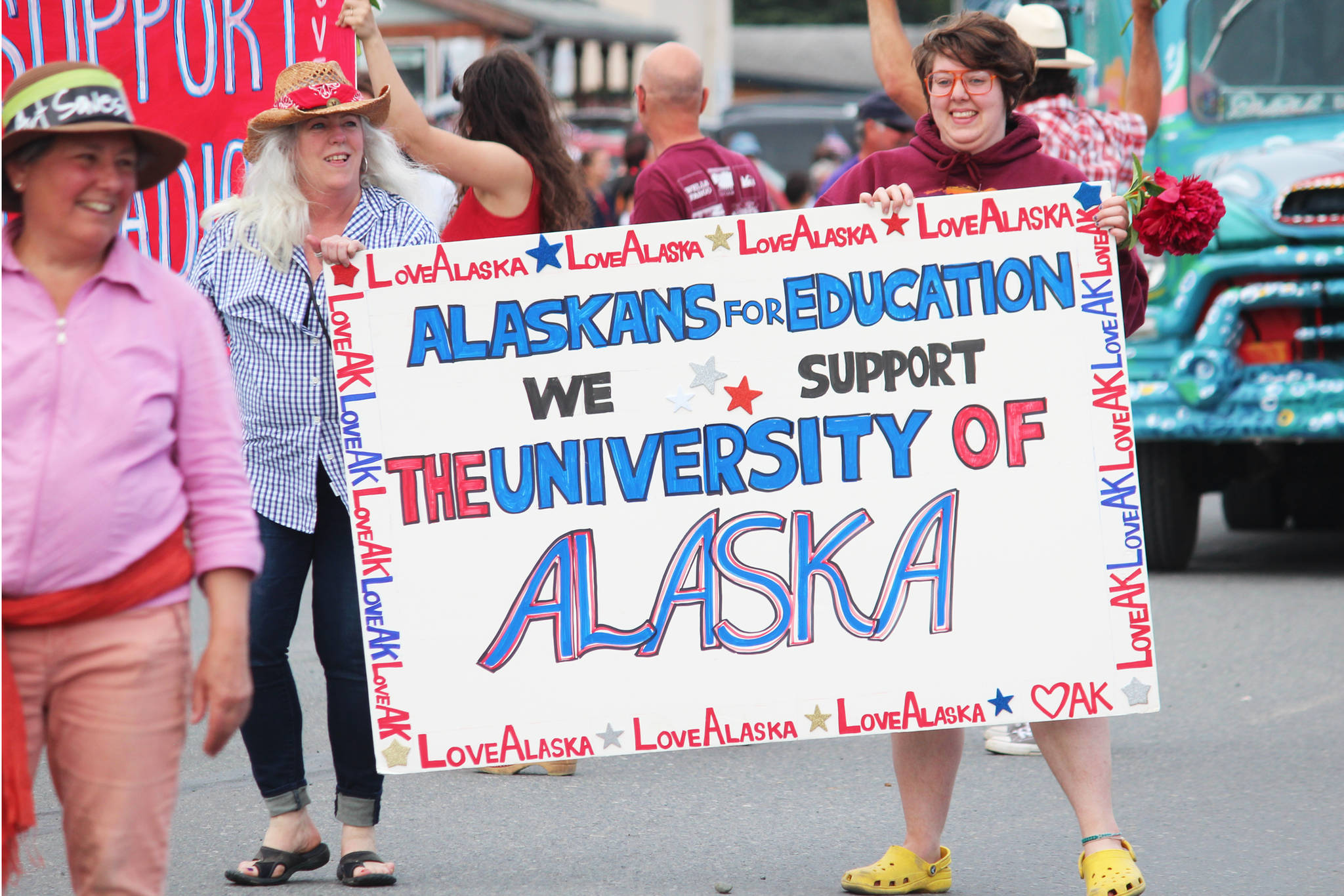 Participants in this year’s July Fourth parade hold a sign supporting the University of Alaska system while marshing down Pioneer Avenue on Thursday, July 4, 2019 in Homer, Alaska. (Photo by Megan Pacer/Homer News)