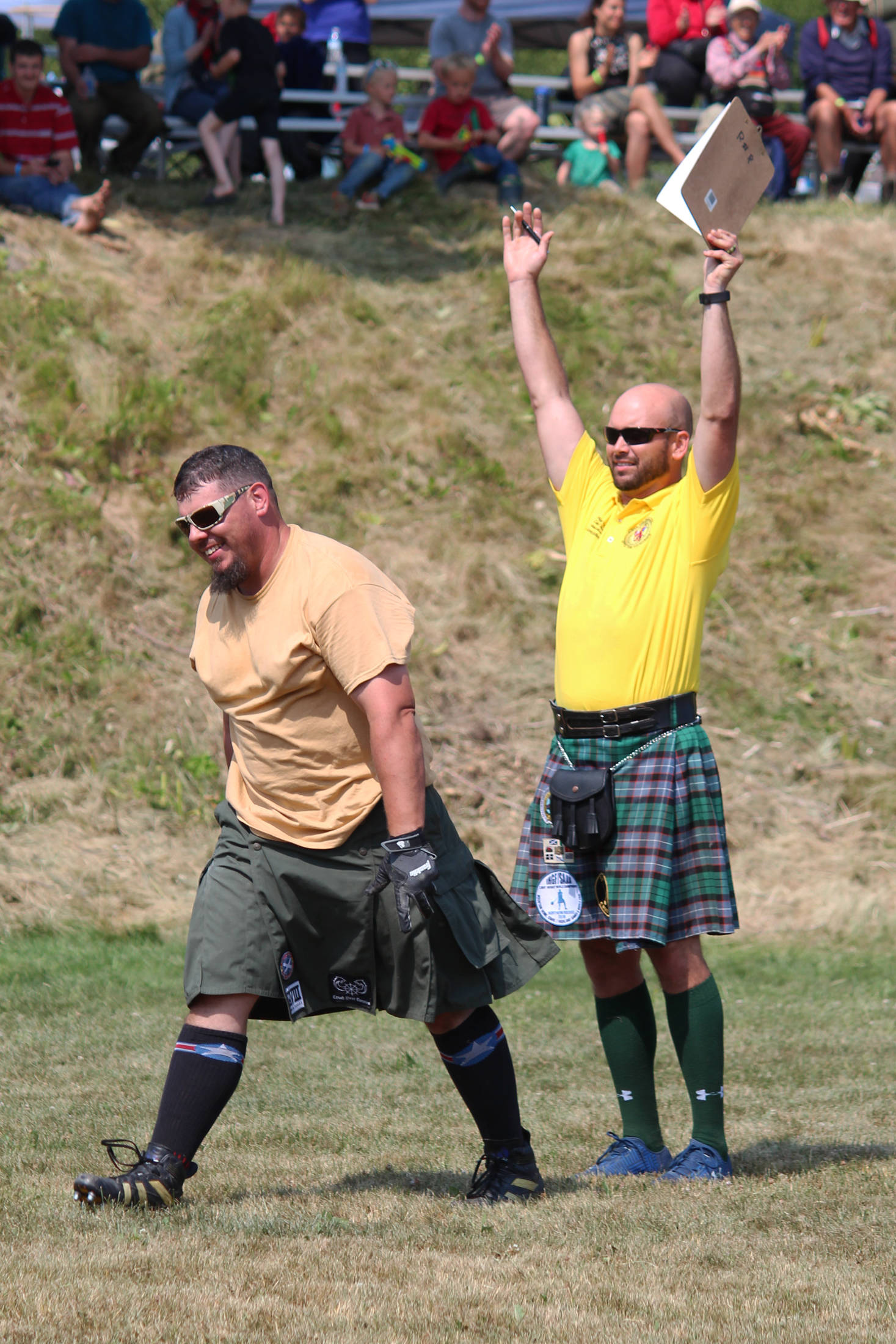 A judge throws his arms into the air to indicate that Danny Autrey, left, earned a perfect score in the men’s caber toss by throwing the caber so that it flipped once and landed in the 12 o’clock position, or directly in front of the athlete, on Saturday, July 6, 2019 at Karen Hornaday Park in Homer, Alaska. Autrey took first place in the Men’s Open class at the annual Kachemak Bay Highland Games held there. (Photo by Megan Pacer/Homer News)