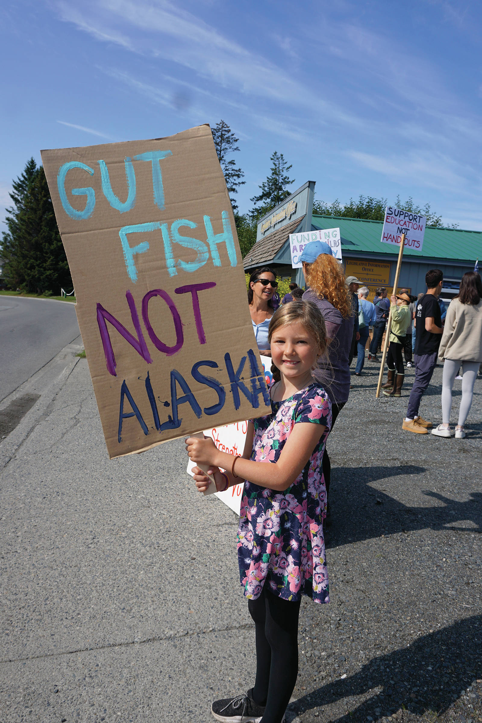 Morgan Harness holds a sign at a rally Sunday, July 28, 2019, against Gov. Mike Dunleavy’s budget cuts at the Legislative Information Office, Homer, Alaska. (Photo by Michael Armstrong/Homer News).