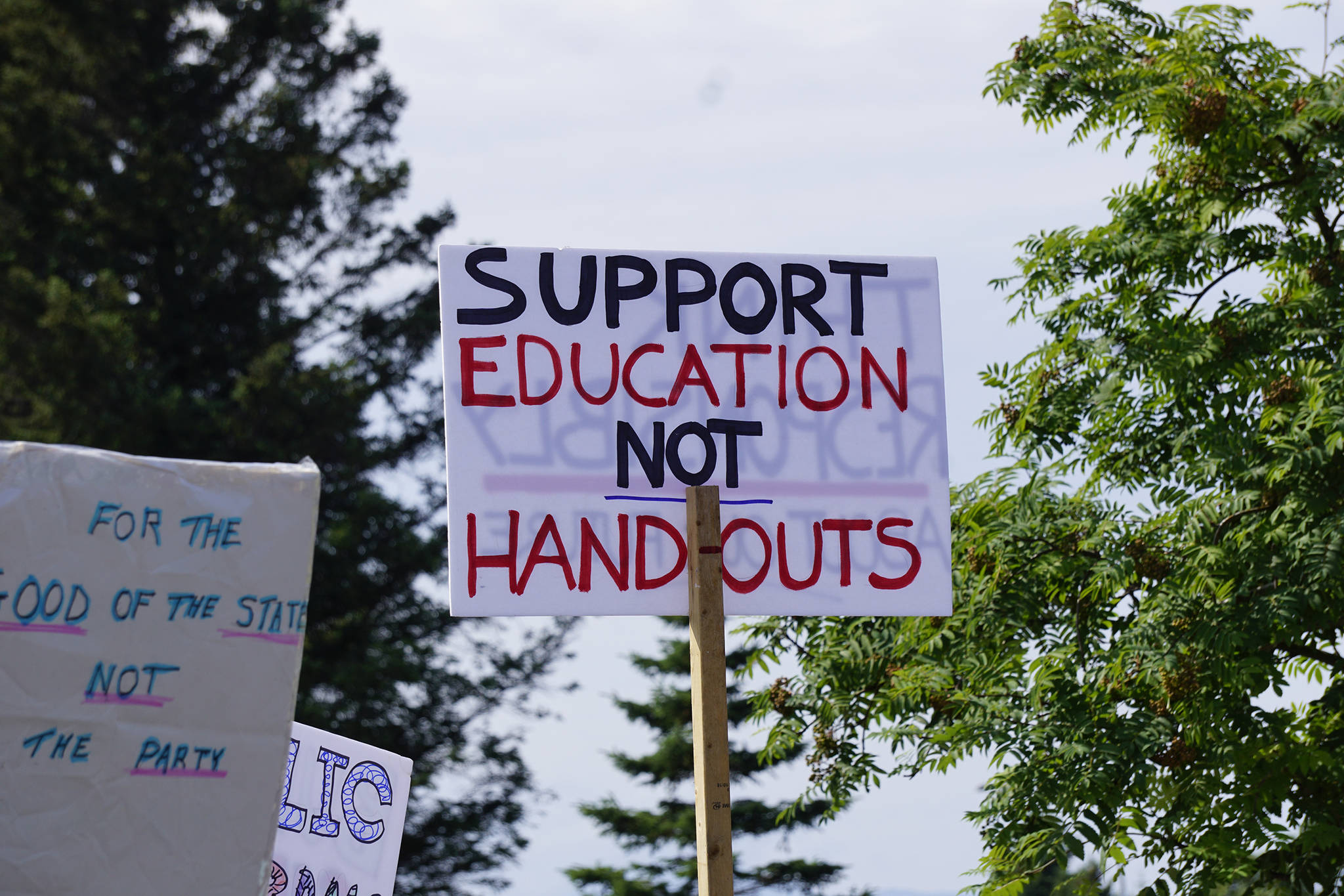 A demonstrator holds a sign at a rally Sunday, July 28, 2019, against Gov. Mike Dunleavy’s budget cuts at the Legislative Information Office, Homer, Alaska. (Photo by Michael Armstrong/Homer News).